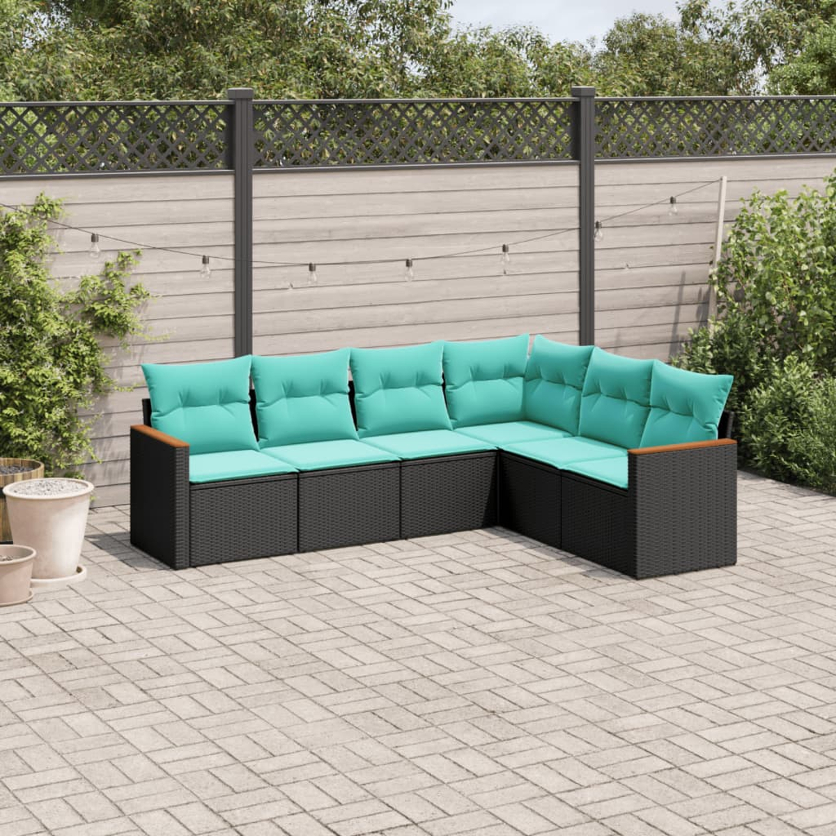 Ein Ecksofa im Freien mit türkisfarbenen Kissen steht auf einer Ziegelterrasse. Ein Holzzaun und Pflanzen sind im Hintergrund.