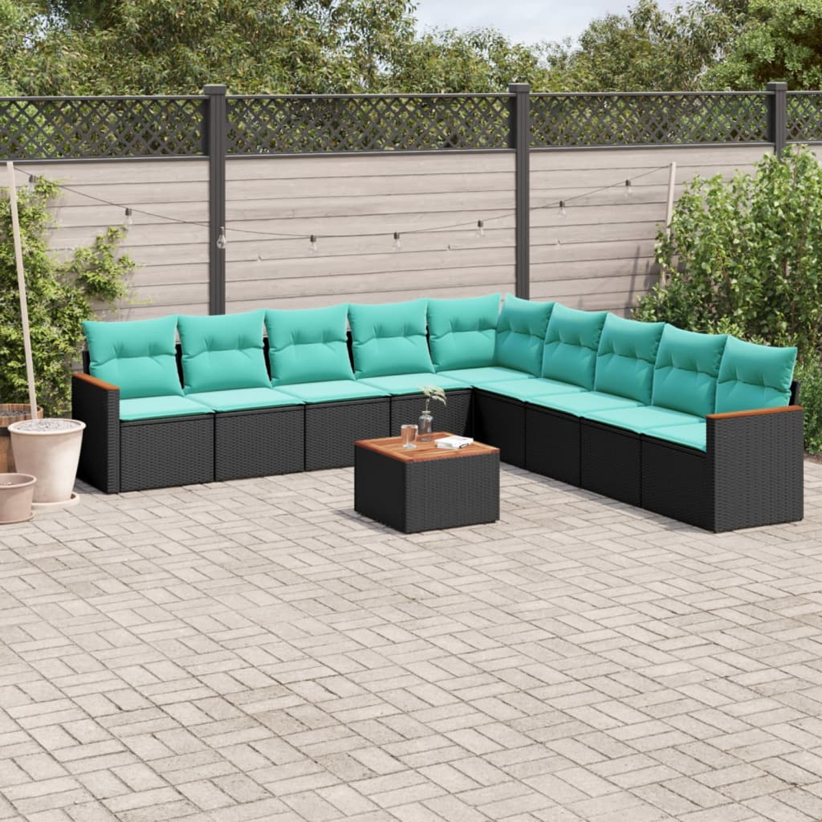 Outdoor-Ecksofa mit türkisfarbenen Kissen und einem kleinen Holztisch steht auf einer Ziegelterrasse. Hintergrund ist ein Zaun und Grün.