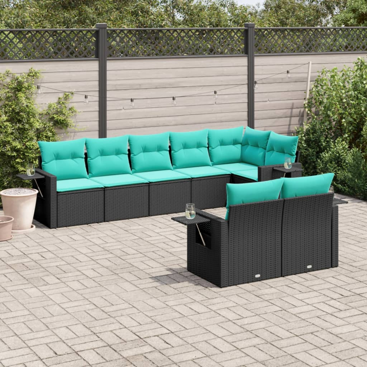 Juego de muebles de patio para exteriores con marcos de mimbre negro y cojines turquesa. Un vaso de agua descansa sobre las mesas laterales.