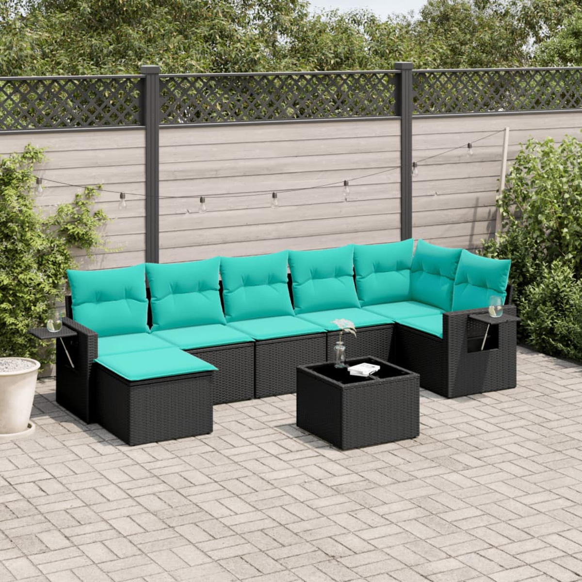 Gartensitzgruppe mit türkisfarbenen Kissen, schwarzem Korbgewebe und passendem Couchtisch. Der Hintergrund zeigt einen Holzzaun und Grün.