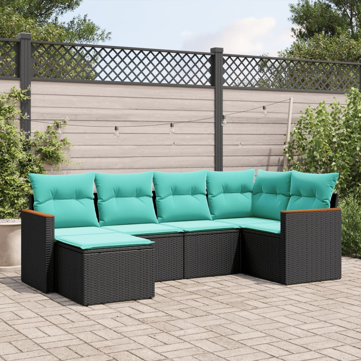Ein Ecksofa im Freien mit türkisfarbenen Kissen steht auf einer Terrasse. Ein Holzzaun und Lichterketten sind im Hintergrund.
