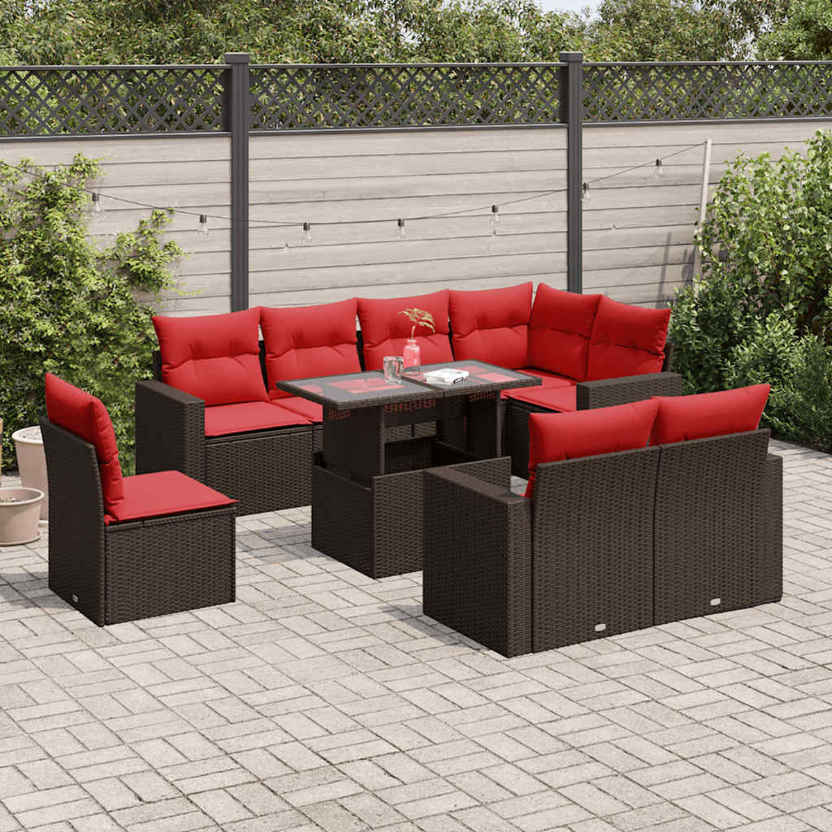 Garten-Terrassenset mit dunkelbraunen Korbmöbeln und roten Kissen. Enthält einen Tisch, ein Ecksofa und Stühle auf einer Steinterrasse.