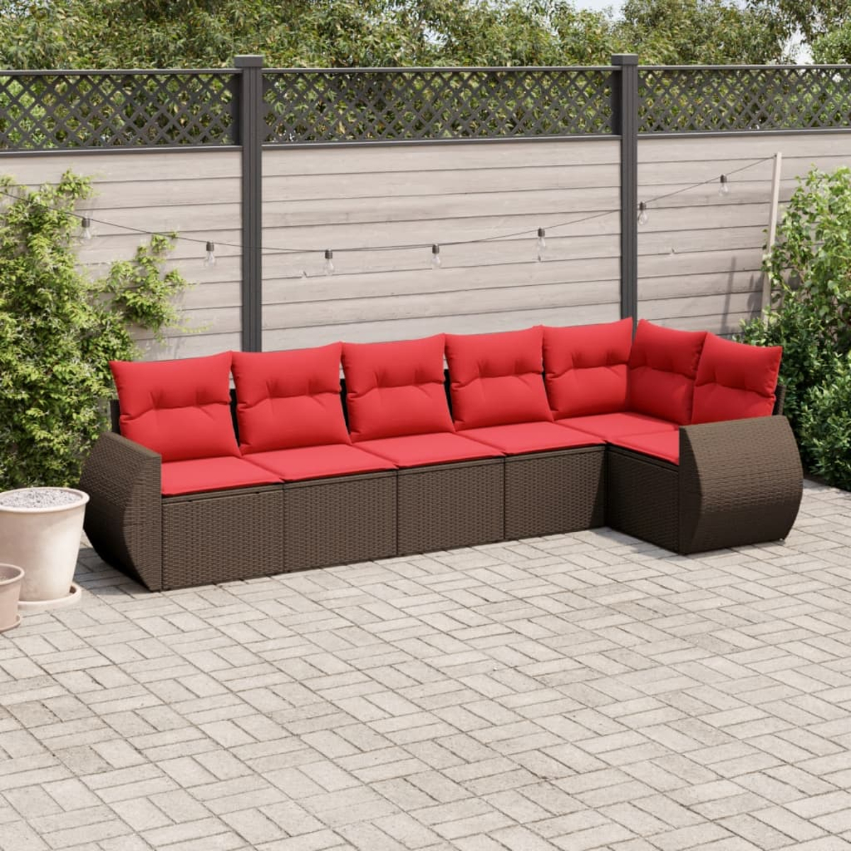 Ein Ecksofa mit roten Kissen steht auf einer Ziegelterrasse. Im Hintergrund befinden sich ein Zaun und Grün.