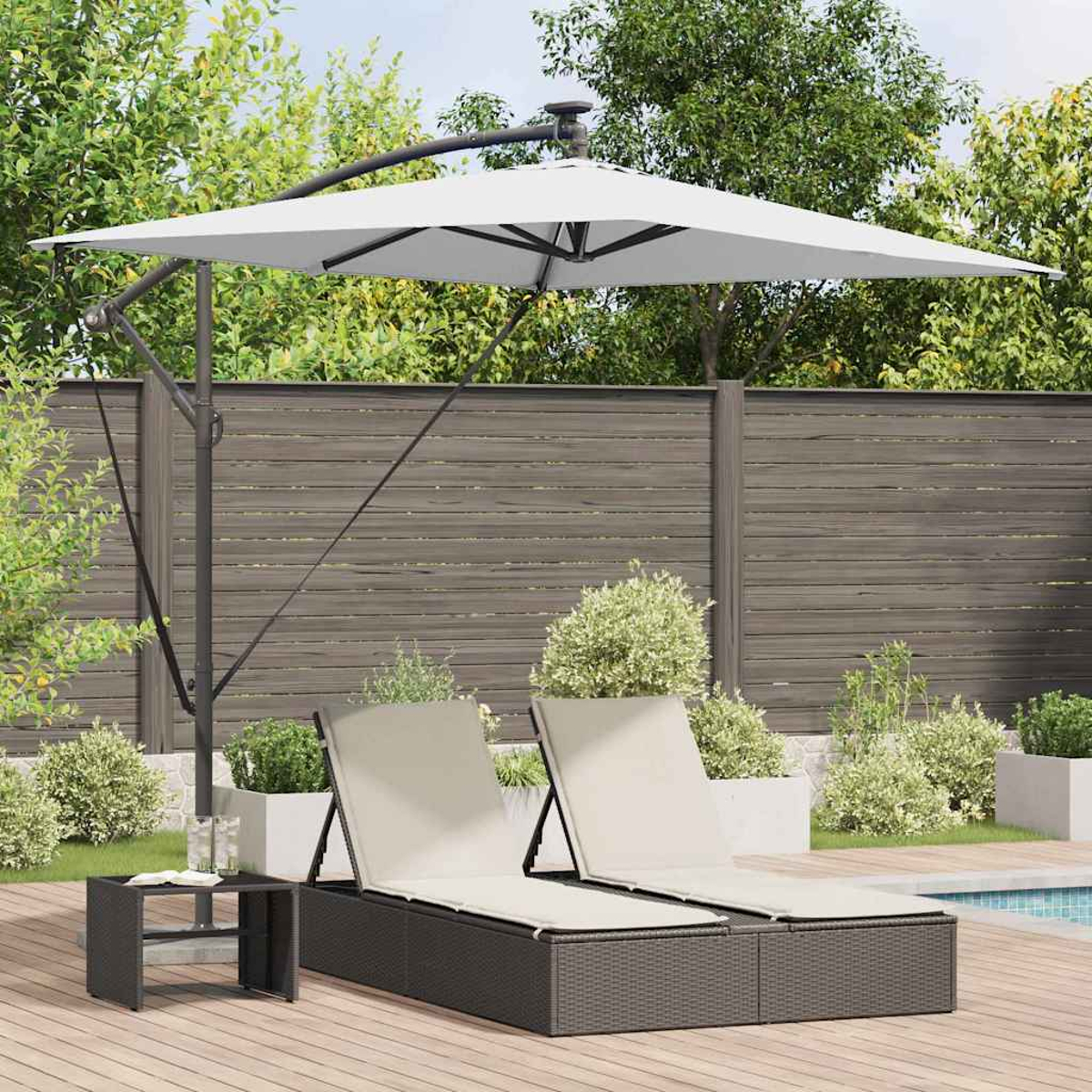 Scena all'aperto con lettini, un tavolo e un grande ombrello bianco. Terrazza in legno, piscina sullo sfondo, alberi e cespugli verdi.