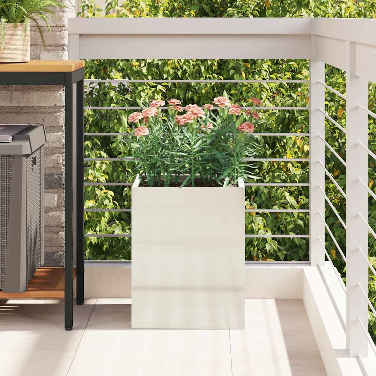 Ein Balkon mit einem weißen Pflanzgefäß mit rosa Blumen, einem Metallgrill und einer Backsteinmauer. Ein weißes Geländer und grünes Laub im Hintergrund.
