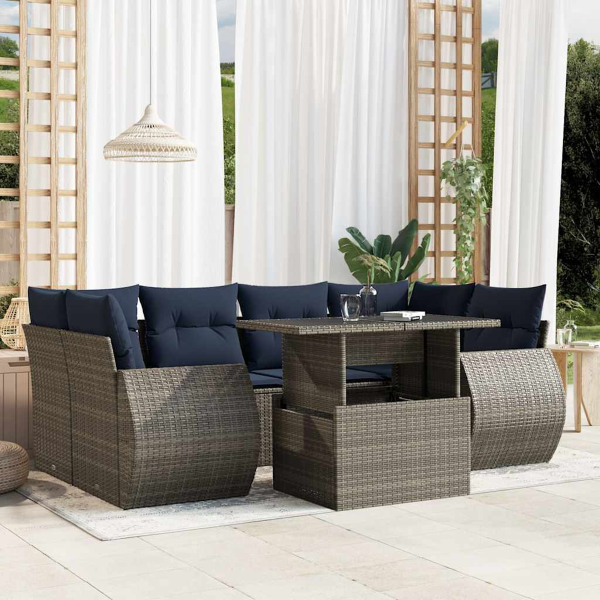 Geflochtenes Gartenmöbel-Set mit marineblauen Kissen. Enthält einen Tisch und Sitzgelegenheiten, weiße Vorhänge und eine Hängelampe.