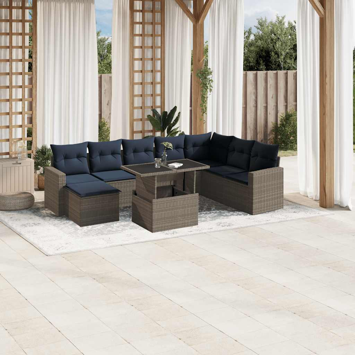 Outdoor-Ecksofa mit marineblauen Kissen, einem ausziehbaren Couchtisch und weißen Vorhängen vor Holzzaun und Grün.