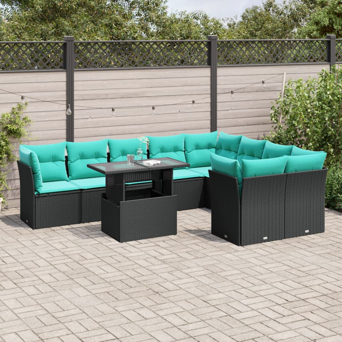 Outdoor-Terrassenset mit schwarzer Korbmöbel und türkisfarbenen Kissen. Ein Tisch mit Glasplatte steht davor. Im Hintergrund ist ein Holzzaun zu sehen.