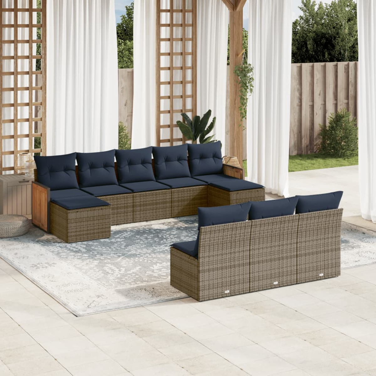 Garten-Sitzgruppe mit blauen Kissen. Korbmöbel auf einer Terrasse, mit Vorhängen und Holzgitter. Hintergrund Bäume und Zaun.
