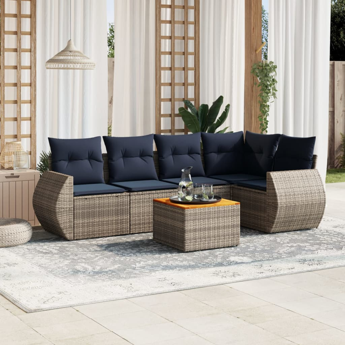 Outdoor-Ecksofa mit marineblauen Kissen und einem quadratischen Couchtisch mit Tablett. Weiße Vorhänge und Spalier im Hintergrund.