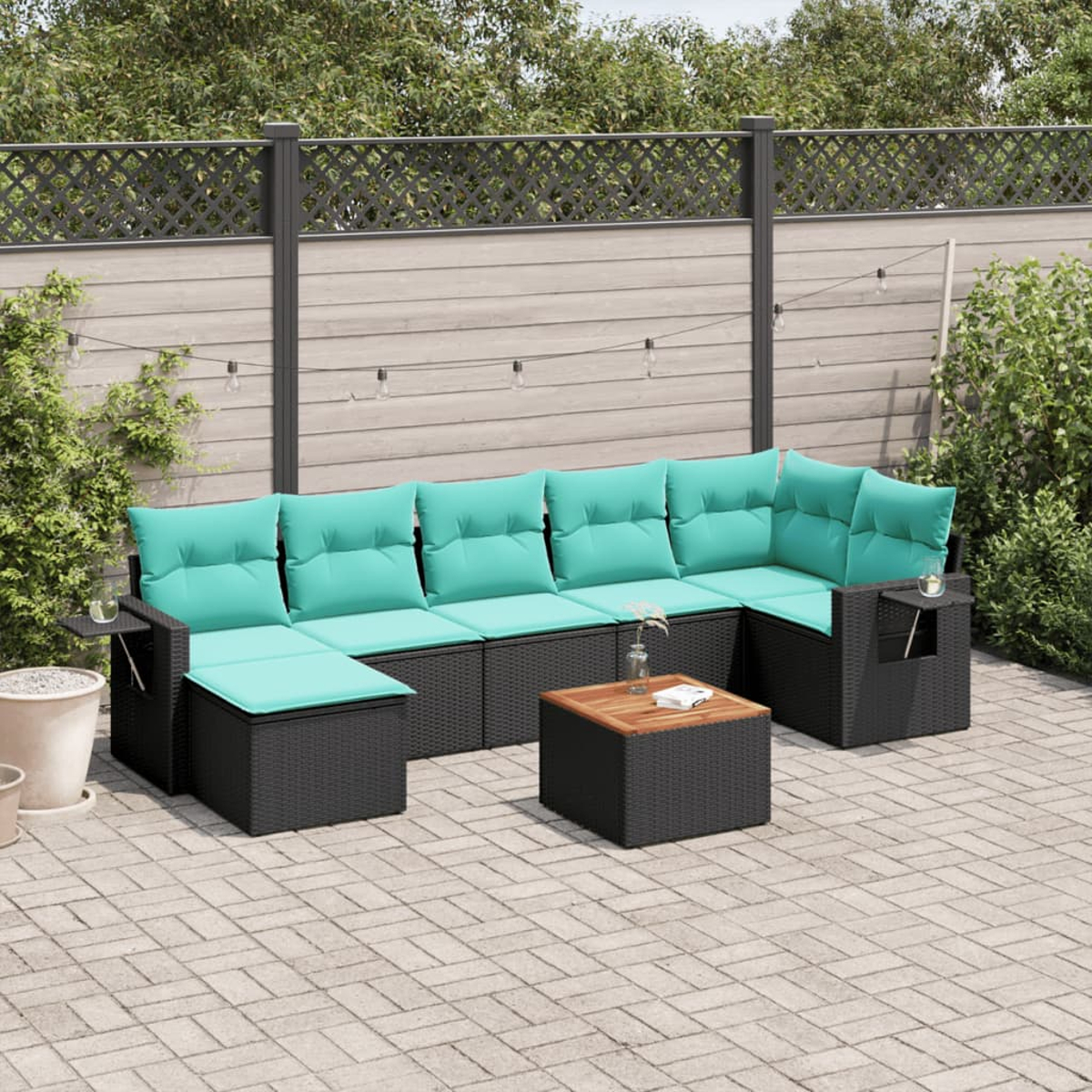 Garten-Sitzgruppe mit türkisfarbenen Kissen. Inklusive Couchtisch und Beistelltischen. Vor einem Holzzaun und Grün.