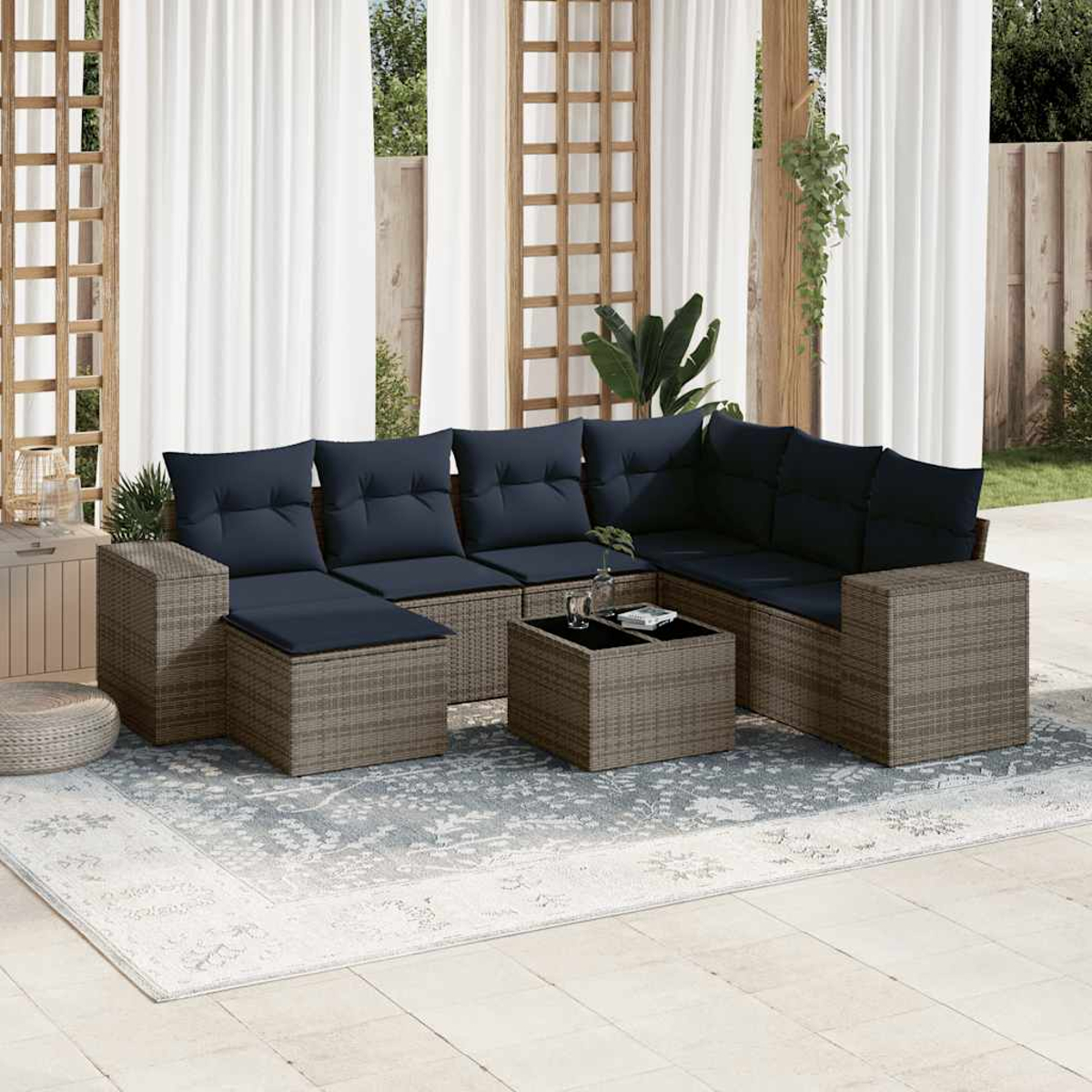 Garten-Sitzgruppe mit blauen Kissen, Couchtisch und Teppich. Weiße Vorhänge und Holzrahmen im Hintergrund. Sonnige, Outdoor-Umgebung.