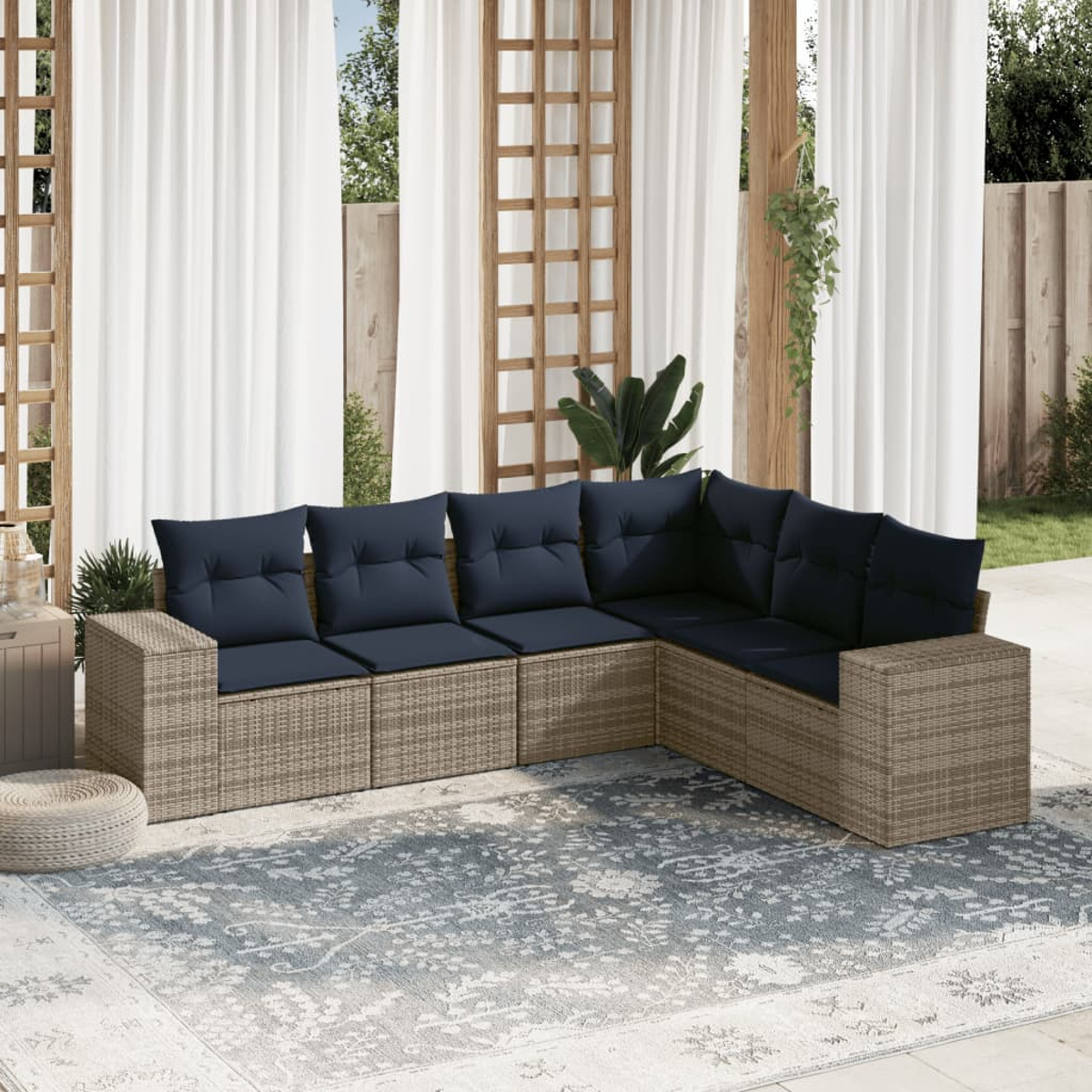 Ein Ecksofa im Freien mit marineblauen Kissen auf einem gemusterten Teppich. Weiße Vorhänge und Holzgitter im Hintergrund.