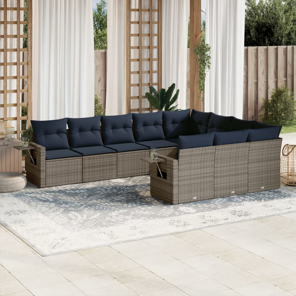 Outdoor-Ecksofa mit marineblauen Kissen auf einem Teppich. Weiße Vorhänge, Holzgitter und Pflanzen im Hintergrund.