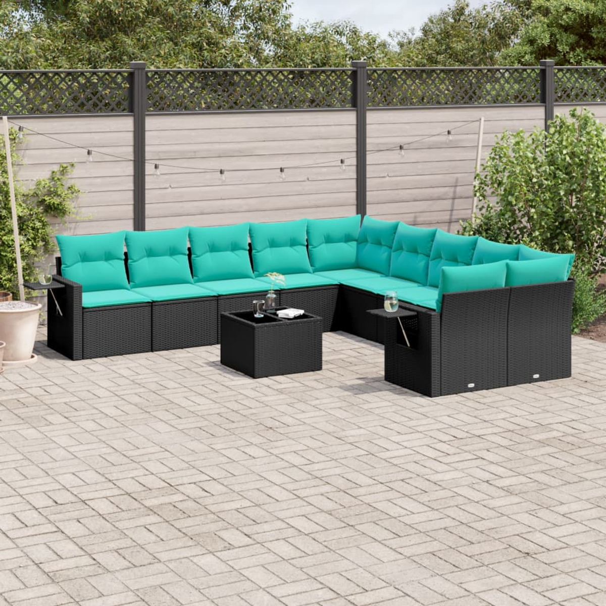 Outdoor-Ecksofa mit türkisfarbenen Kissen und einem schwarzen Tisch. Ziegel-Patio, Holzzaun und Grün im Hintergrund.