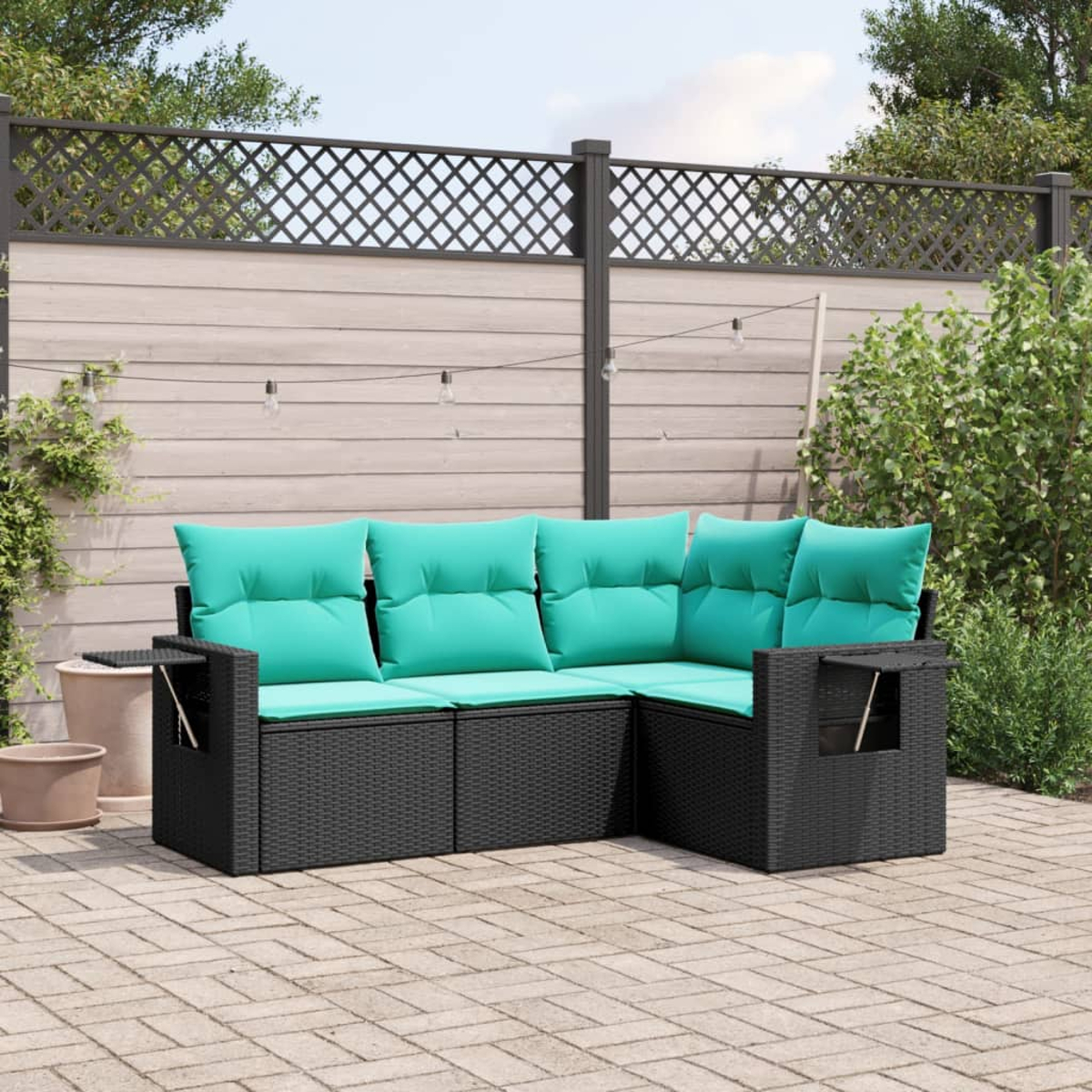 Ein schwarzes Ecksofa aus Weidengeflecht mit türkisfarbenen Kissen steht auf einer Backstein-Terrasse. Im Hintergrund sind ein Holzzaun und Grünflächen zu sehen.