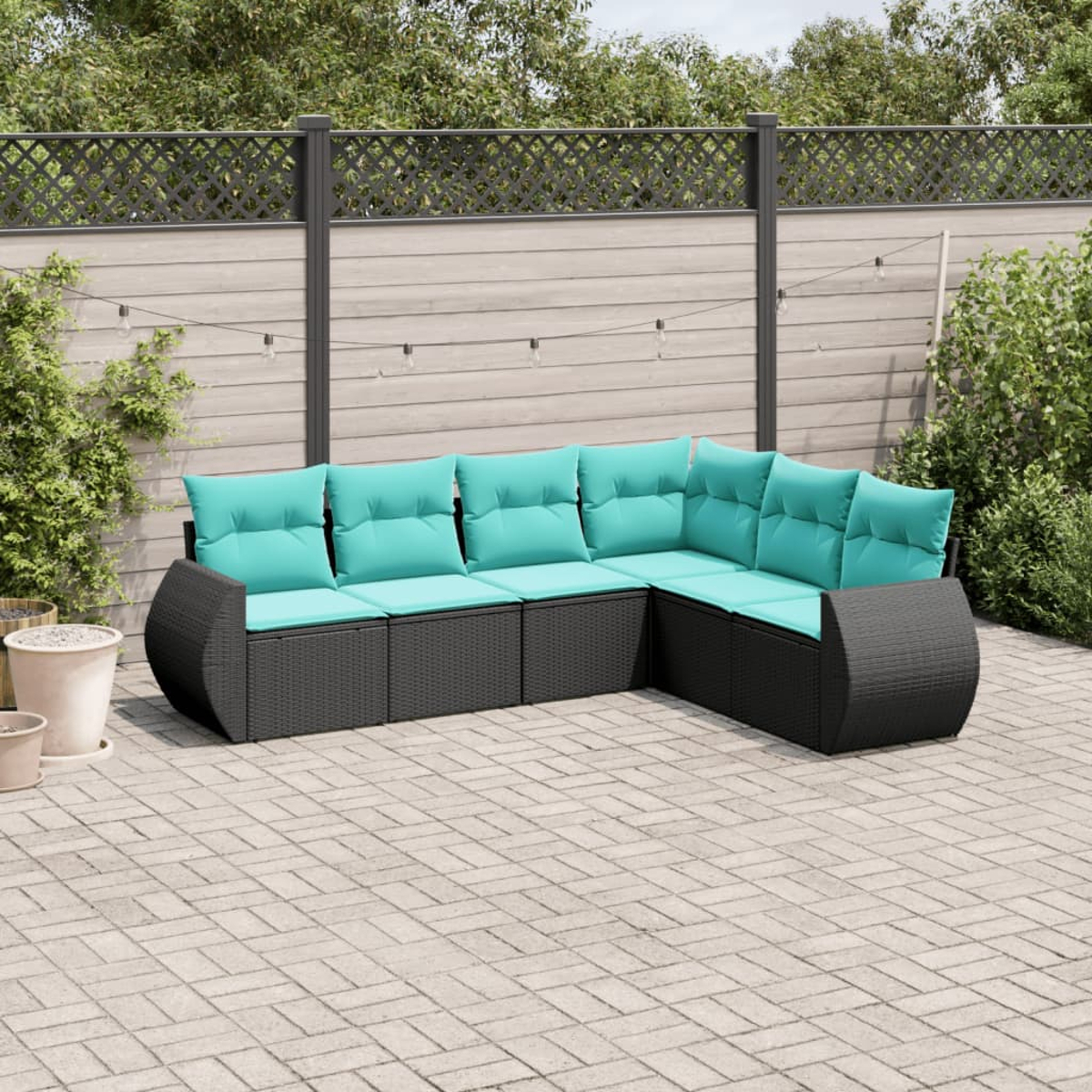 Un sofá seccional para exteriores con cojines turquesa. Los muebles de mimbre negro están en un patio. Una valla y vegetación al fondo.