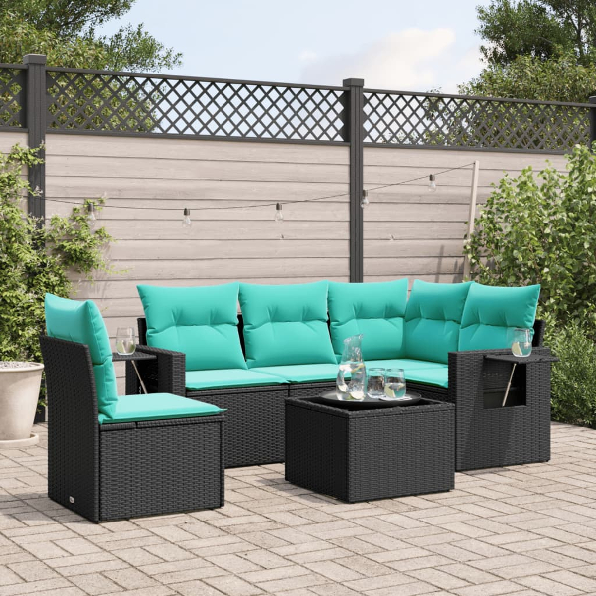 Gartenmöbel-Set mit türkisfarbenen Kissen auf einer Terrasse. Enthält ein Sofa, einen Stuhl und einen Couchtisch. Holzzaun im Hintergrund.