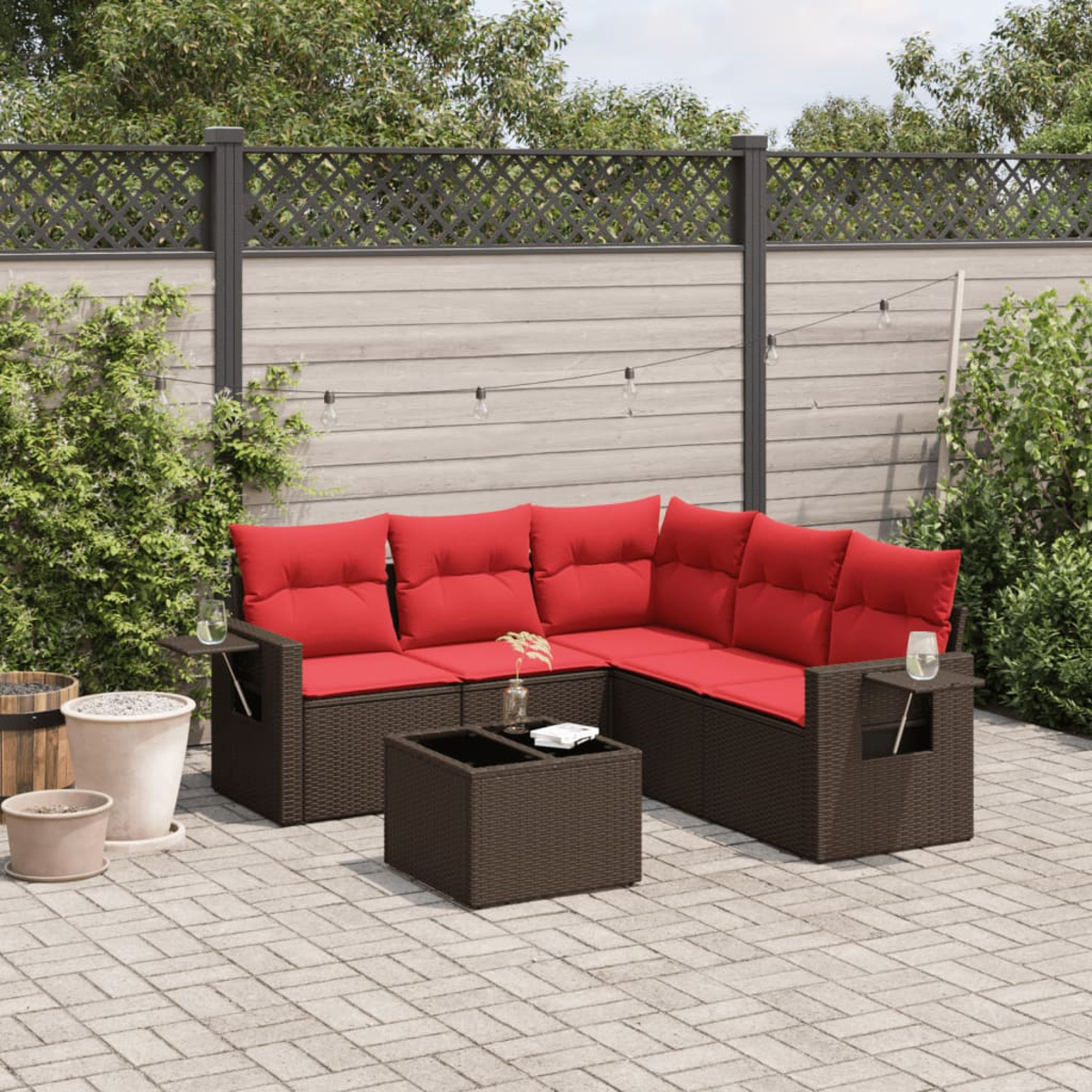 Szene im Freien mit einem braunen Ecksofa aus Korbgeflecht mit roten Kissen, einem Couchtisch, Pflanzen und einem Zaun.