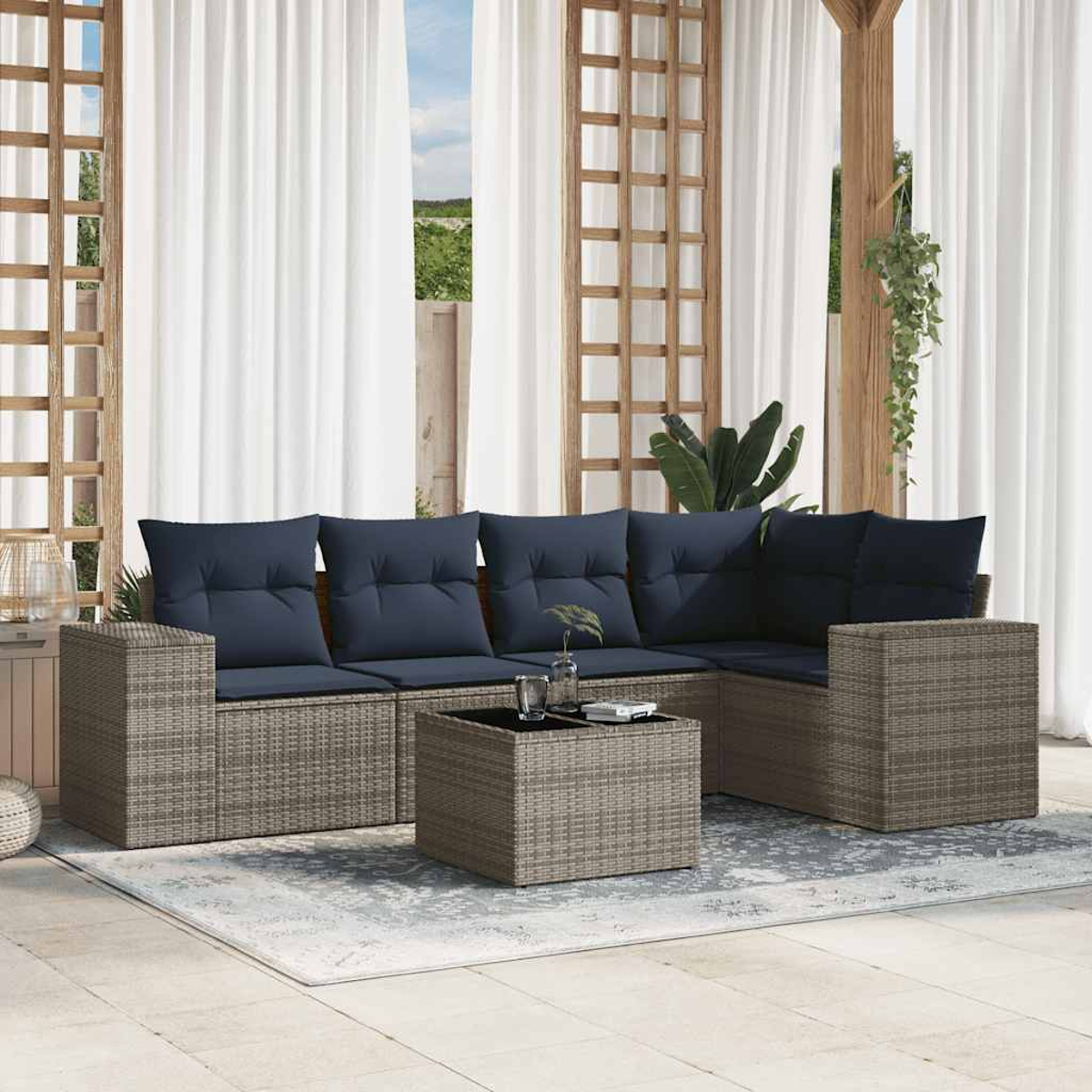 Outdoor-Sitzgruppe mit blauen Kissen. Ein quadratischer Couchtisch und ein Teppich vor weißen Vorhängen.