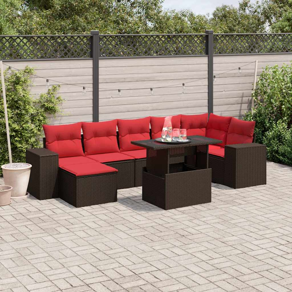 Garten-Terrassenset mit roten Kissen, einem dunklen Tisch und einer hellen Backstein-Terrasse. Im Hintergrund befinden sich ein Zaun und Grün.