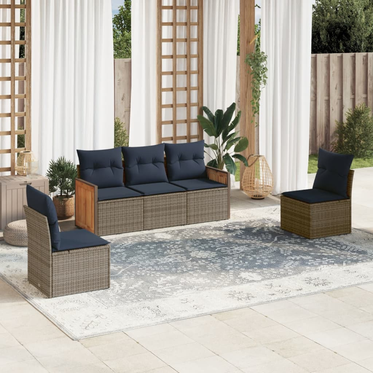 Terrassenset im Freien mit Sofa, zwei Stühlen mit marineblauen Kissen, auf einem gemusterten Teppich. Weiße Vorhänge und Pflanzen im Hintergrund.