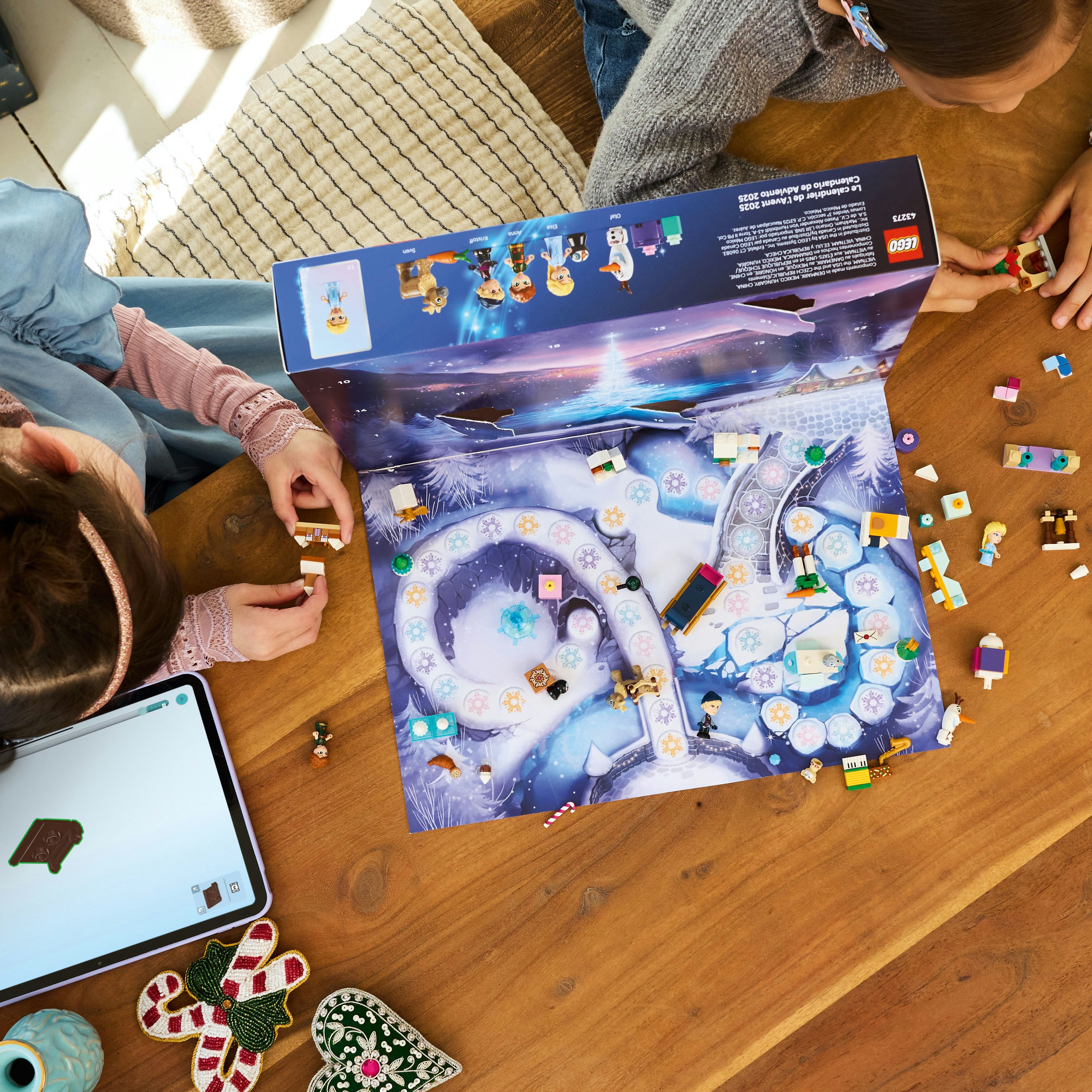 Kinder spielen an einem Holztisch mit Lego. Ein Adventskalender im Frozen-Design ist geöffnet. Verschiedene Lego-Teile sind verstreut.