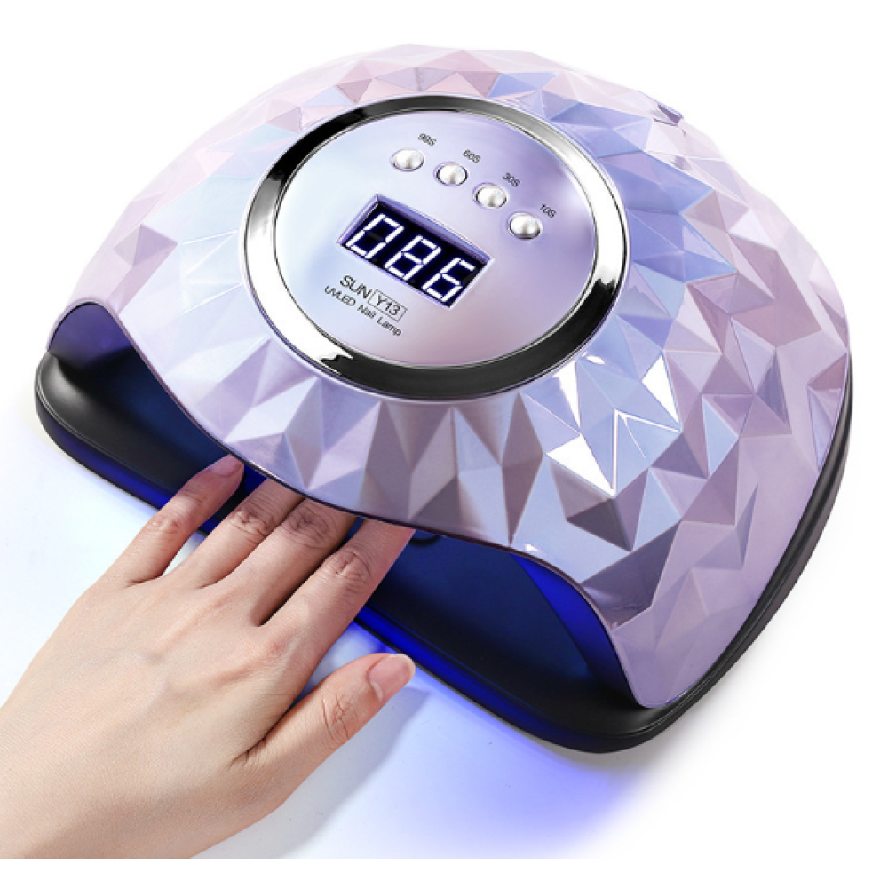 Eine Hand in einer Nagellampe. Die Lampe ist helllila und hat eine Digitalanzeige mit 086. Die Hand ist hell, mit Nägeln.