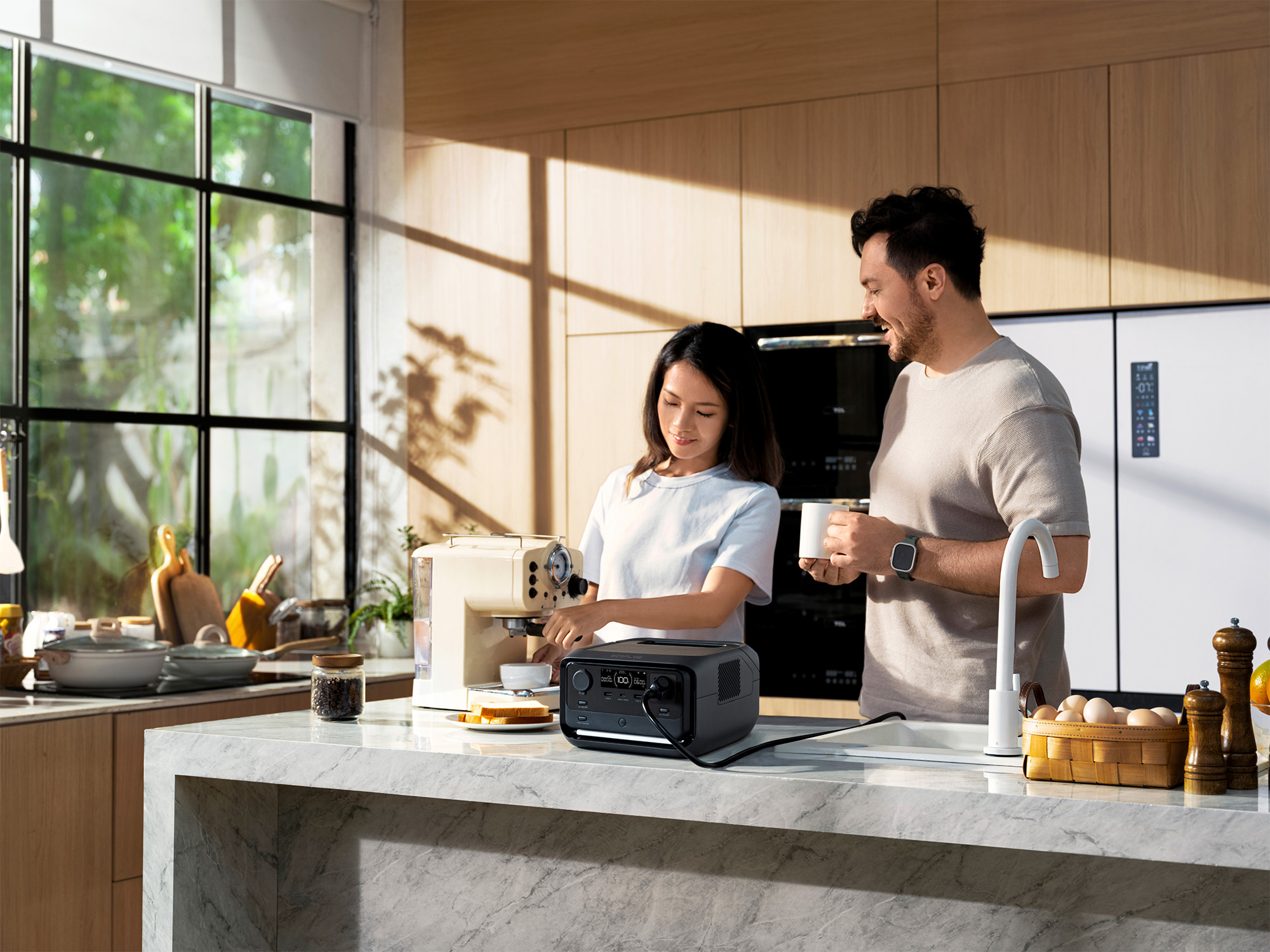 Eine Frau bedient eine Kaffeemaschine. Ein Mann hält einen Becher. Küche mit Geräten und Fenster.