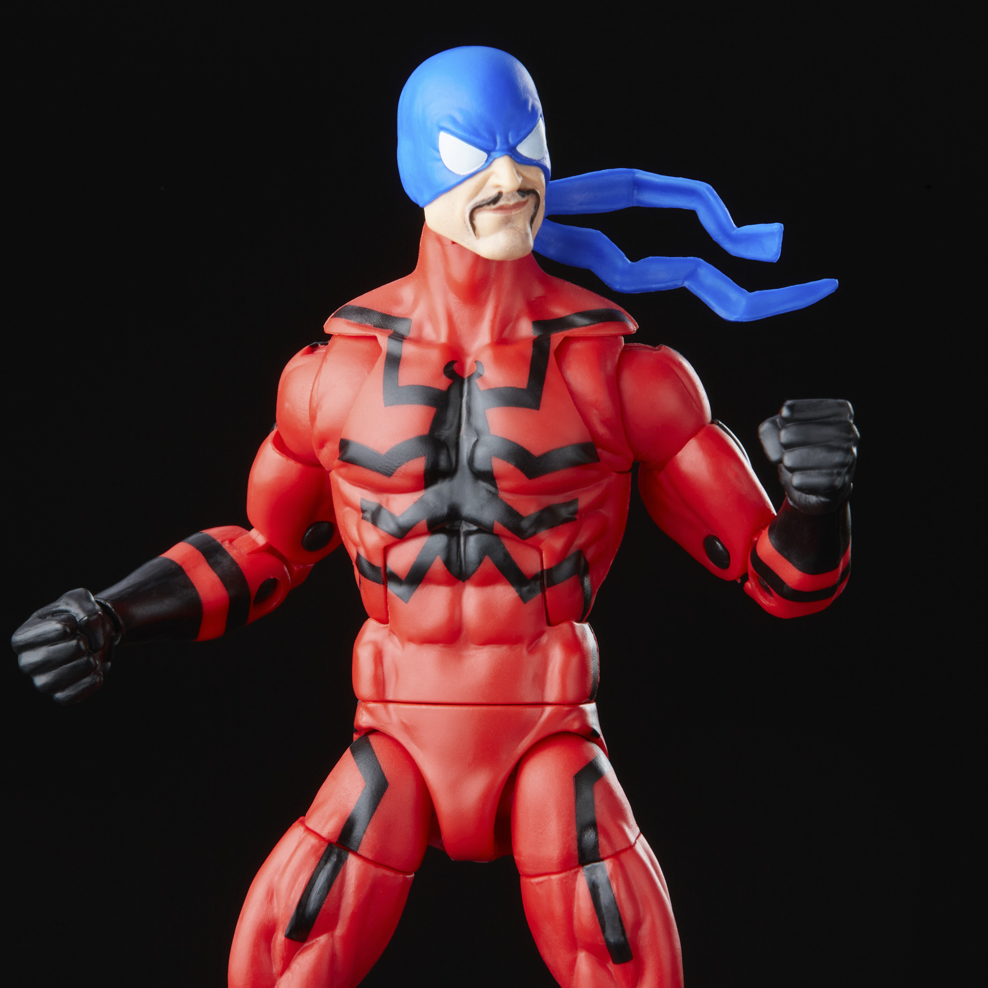 Figura de superhéroe en rojo y negro, con gorro azul y detalles azules, sobre fondo negro.