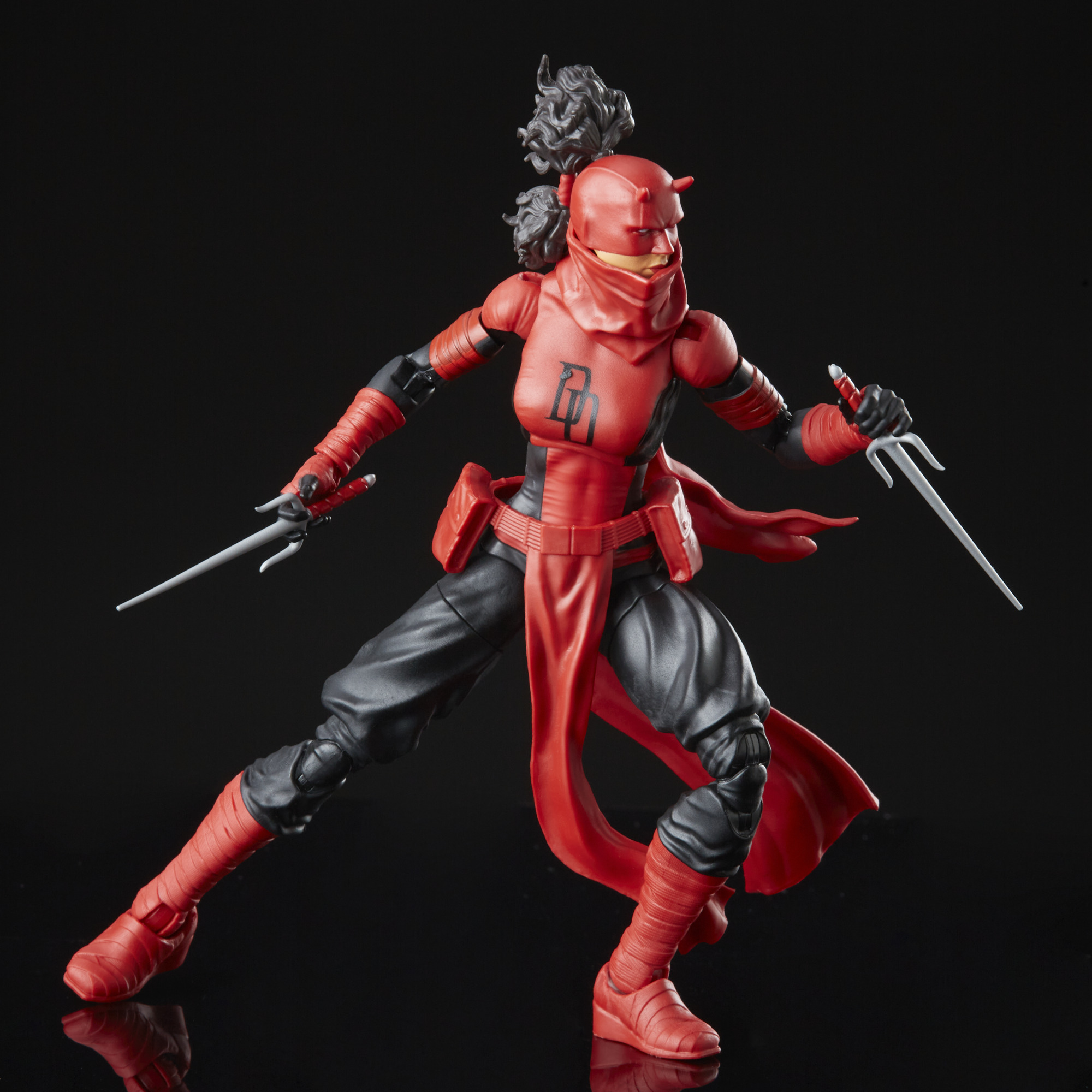 Una figura de acción de Daredevil roja y negra con armas sai. La figura está posada dinámicamente sobre un fondo negro reflectante.