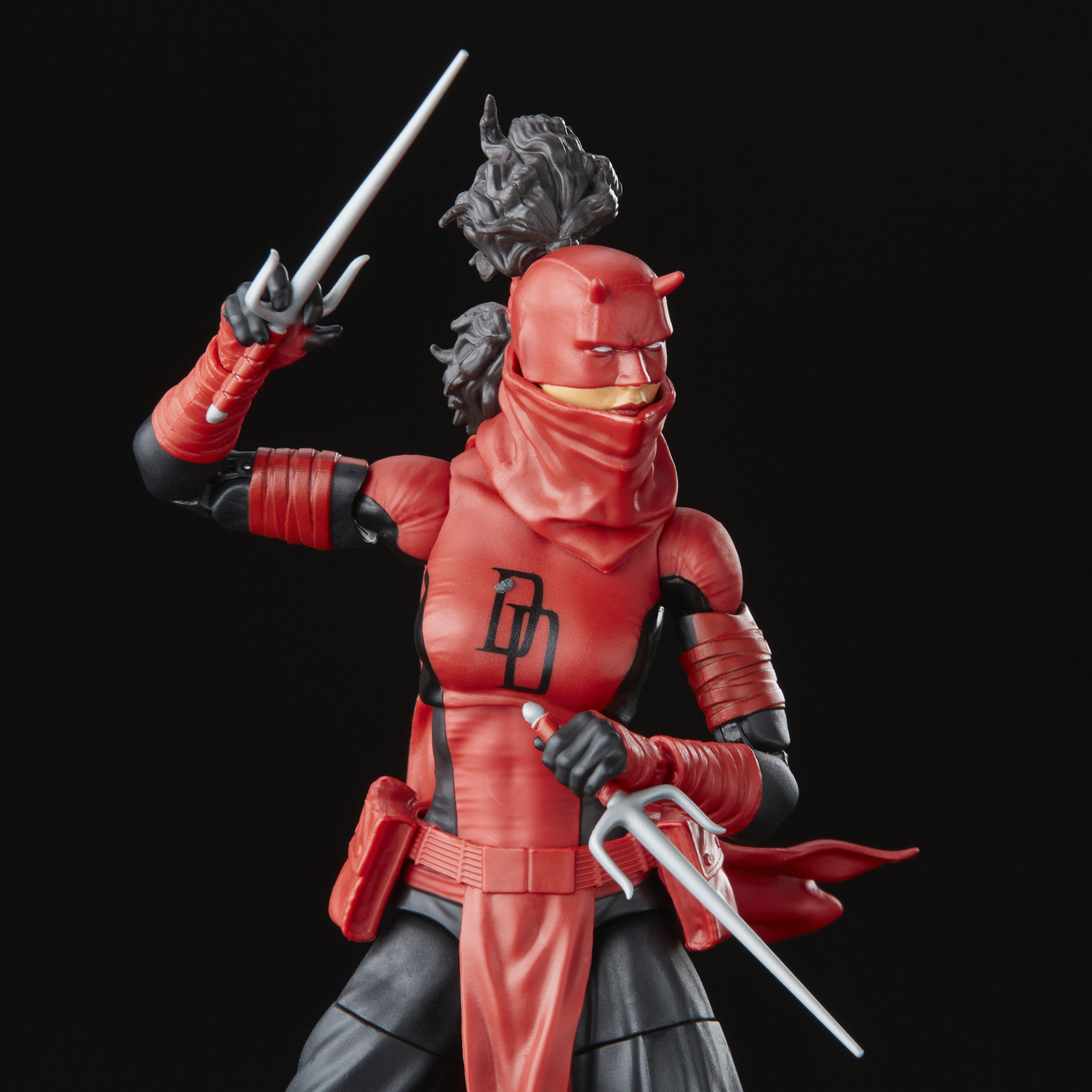 Figura de acción de Daredevil, traje rojo con cuernos, sosteniendo armas sai. Fondo negro.