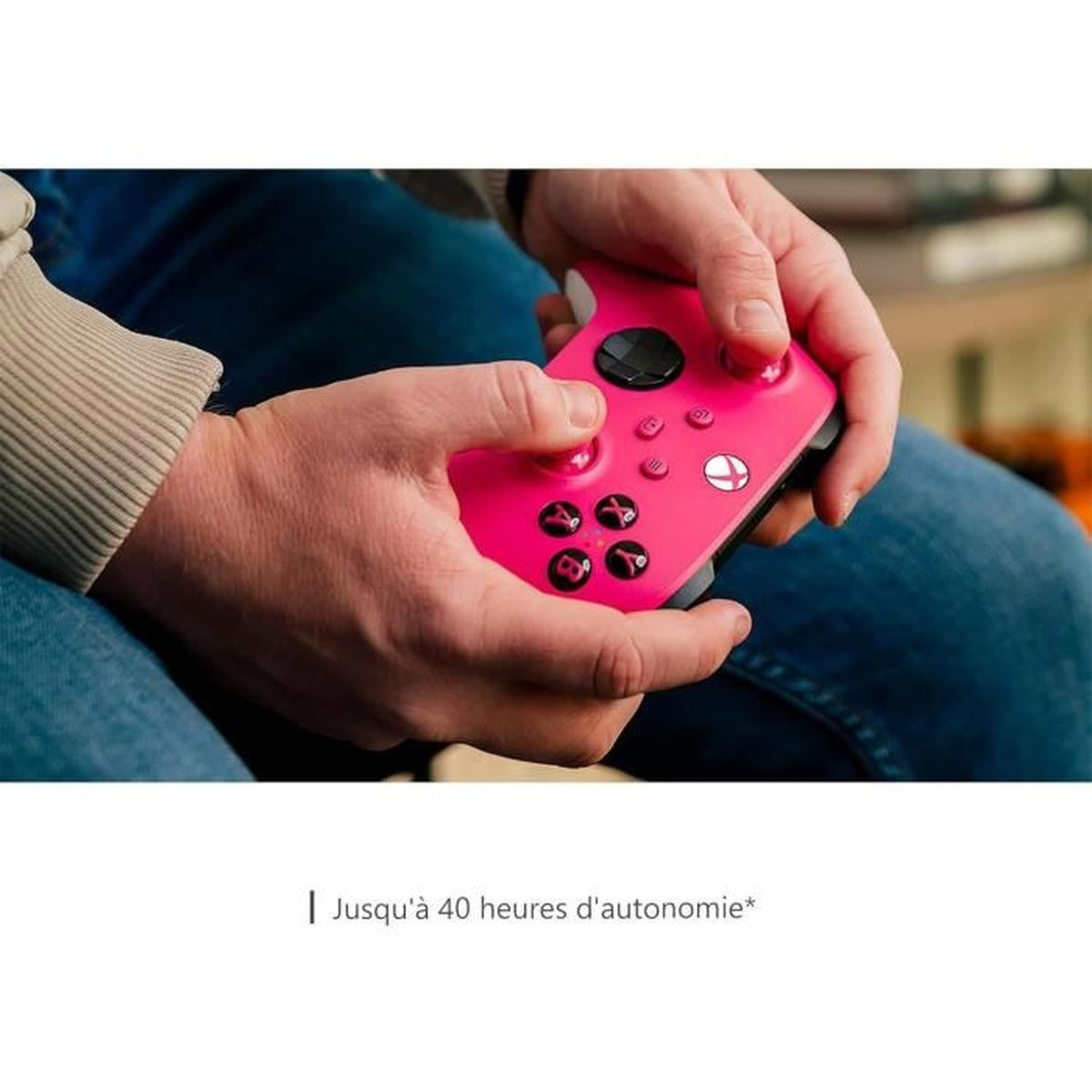 Handen houden een roze gamecontroller vast met zwarte knoppen. De persoon draagt een beige shirt met lange mouwen en een blauwe spijkerbroek.