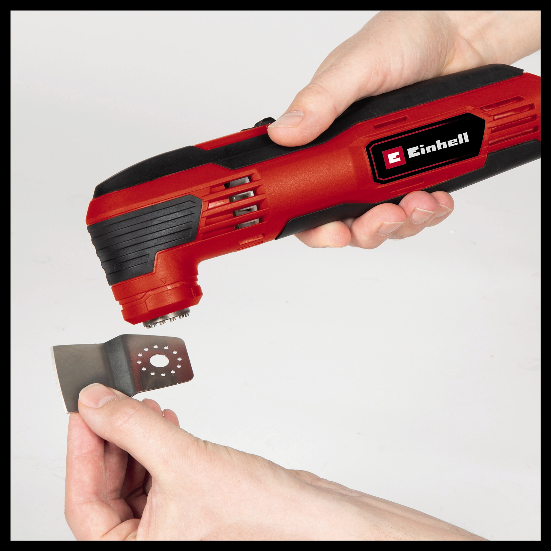 Osoba trzyma czerwono-czarne narzędzie wielofunkcyjne Einhell, odłączając metalowe ostrze z wieloma otworami.