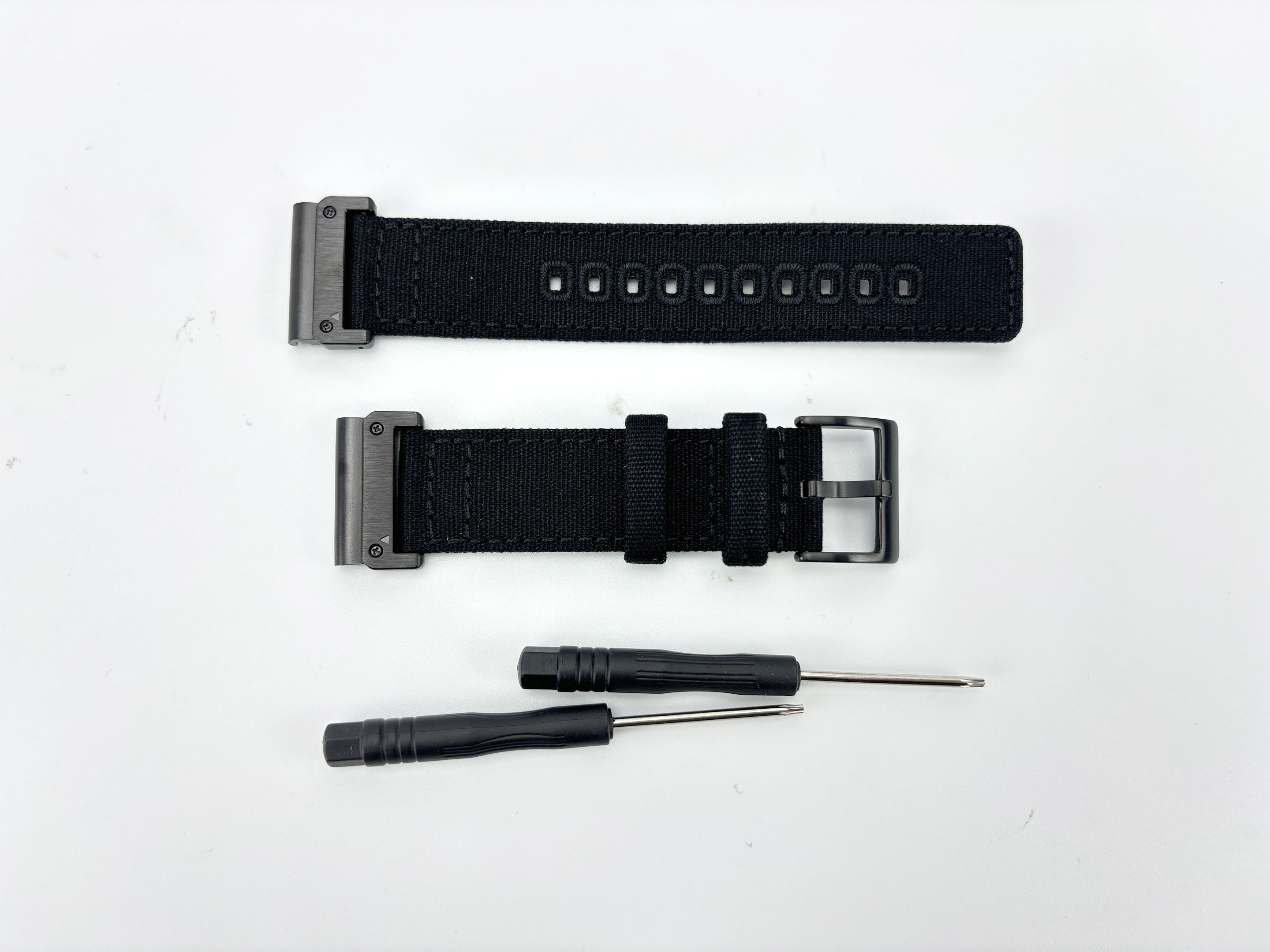 Das Bild zeigt zwei schwarze Uhrenarmbänder und zwei kleine Schraubendreher auf weißem Hintergrund. Die Armbänder sind neu.
