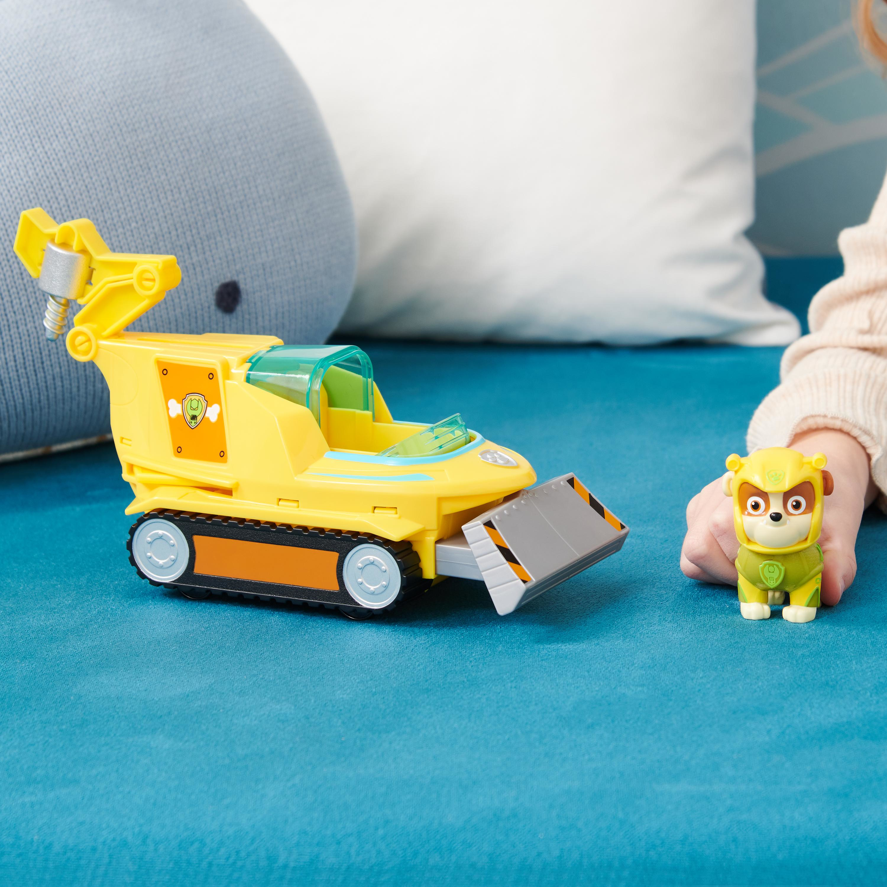 Ein gelber Spielzeugbulldozer und ein gelber Hundespielzeug. Die Hand eines Kindes ist in der Nähe des Hundes. Hintergrund hat blaue und weiße Farben.