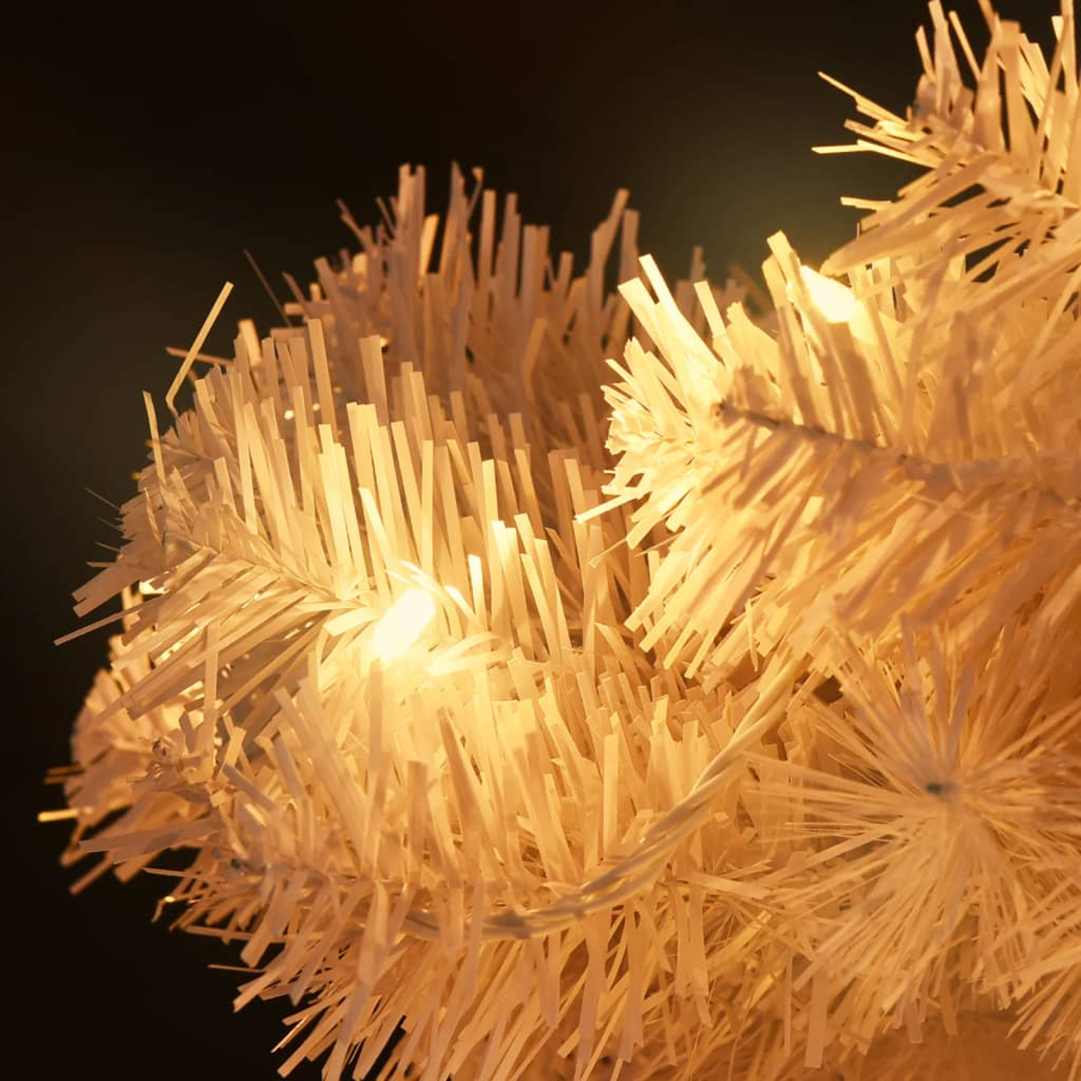 Nahaufnahme eines weißen Weihnachtsbaums mit Lichterketten vor dunklem Hintergrund. Äste sind hell und stachelig.