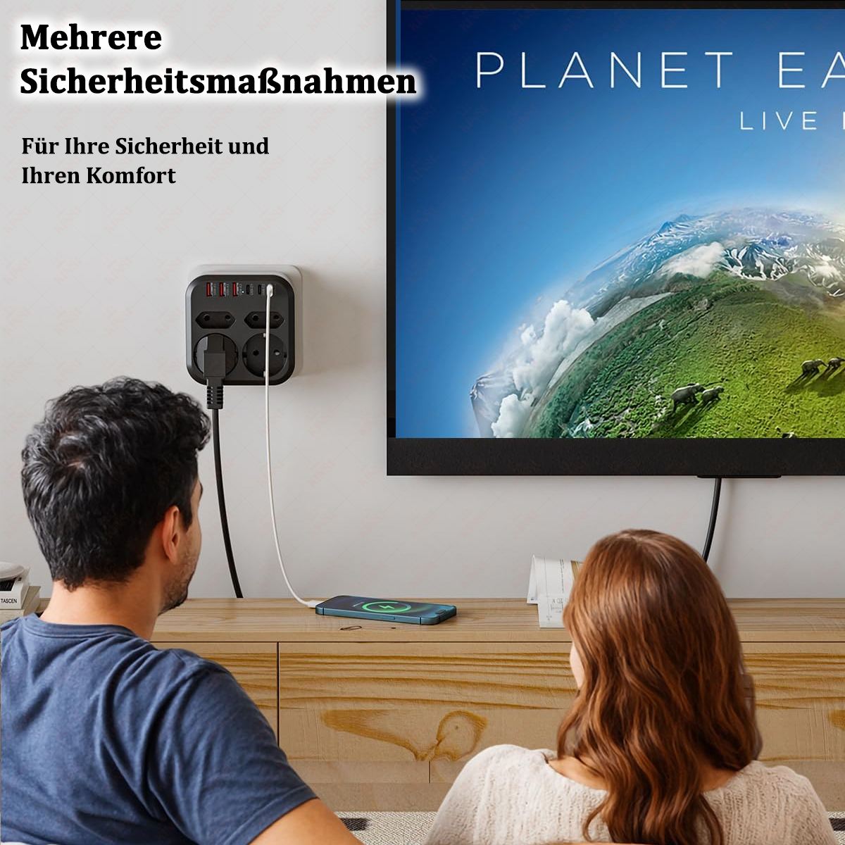 Ein Paar schaut fern. Eine Steckdosenleiste ist an der Wand. Ein Telefon lädt auf dem Tisch.