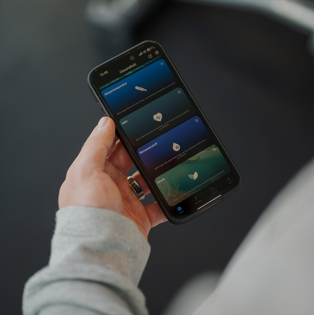 Eine Hand hält ein Telefon mit Gesundheitsmetriken. Der Bildschirm zeigt Körpertemperatur, HRV, Blutsauerstoff und Druck.
