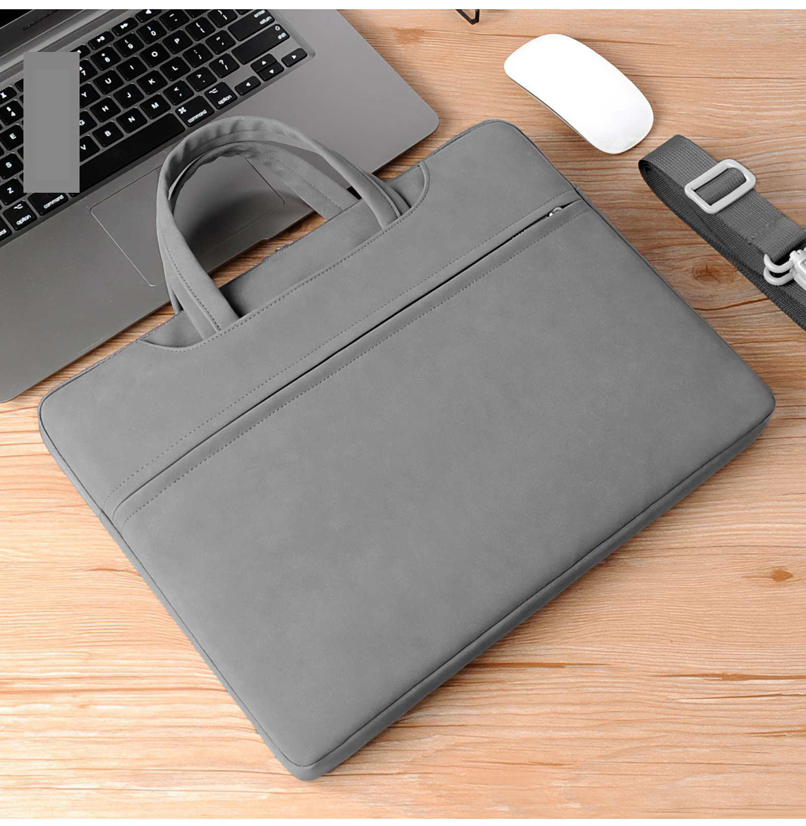 Graue Laptoptasche mit Griffen, Laptop teilweise sichtbar, weiße Maus und Gurt auf Holzoberfläche.