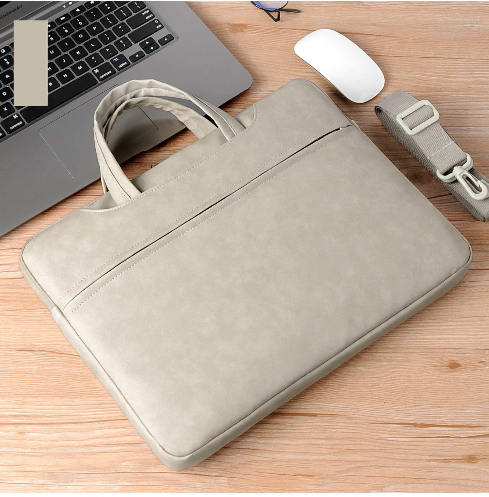 Eine hellgraue Laptoptasche mit Griff liegt auf einem Holztisch, neben einem Laptop, einer Maus und einem Gurt.