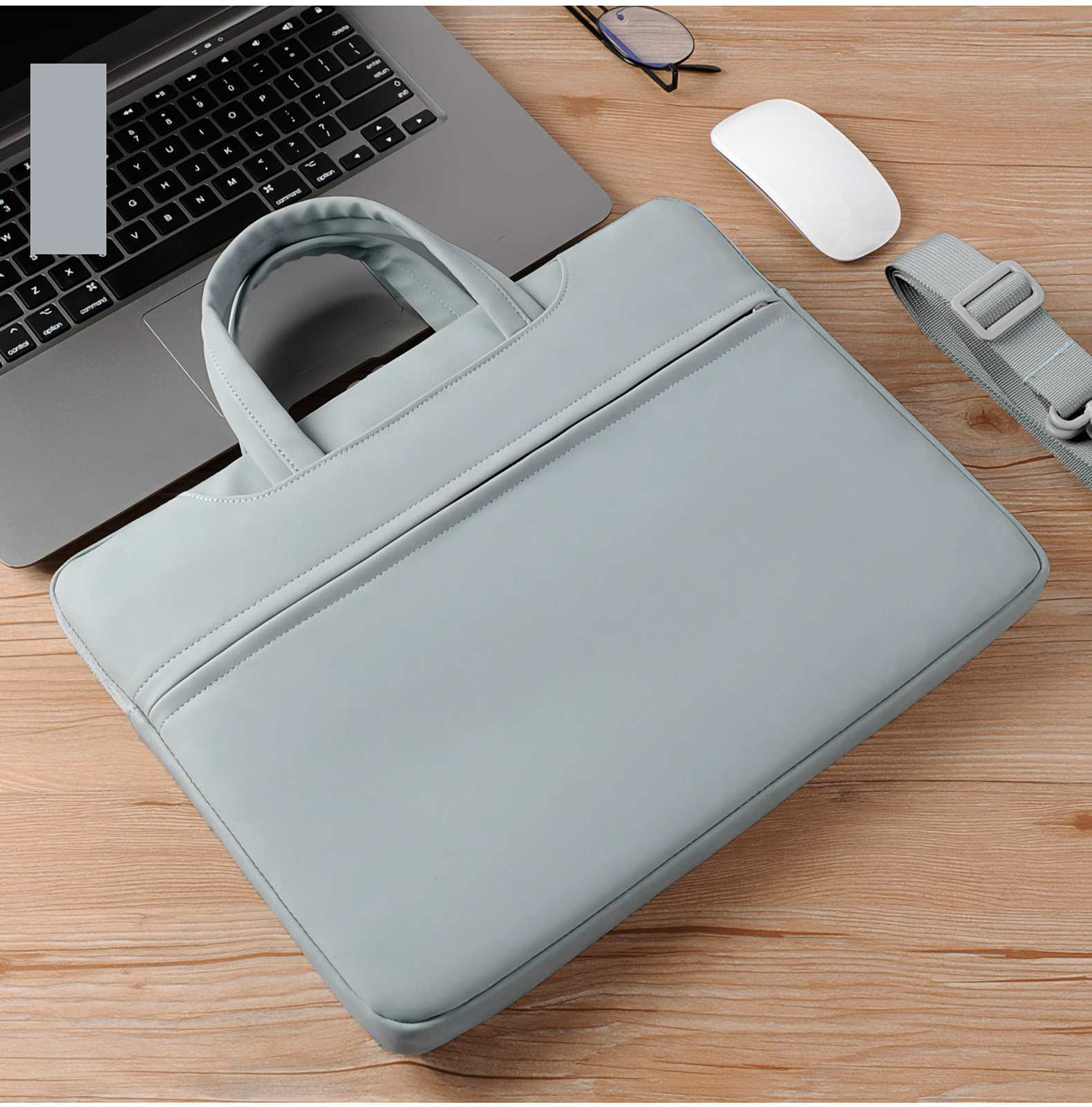 Laptoptasche, Computer, Maus und Brille auf Holzoberfläche. Die Tasche ist grau, der Laptop ist offen.