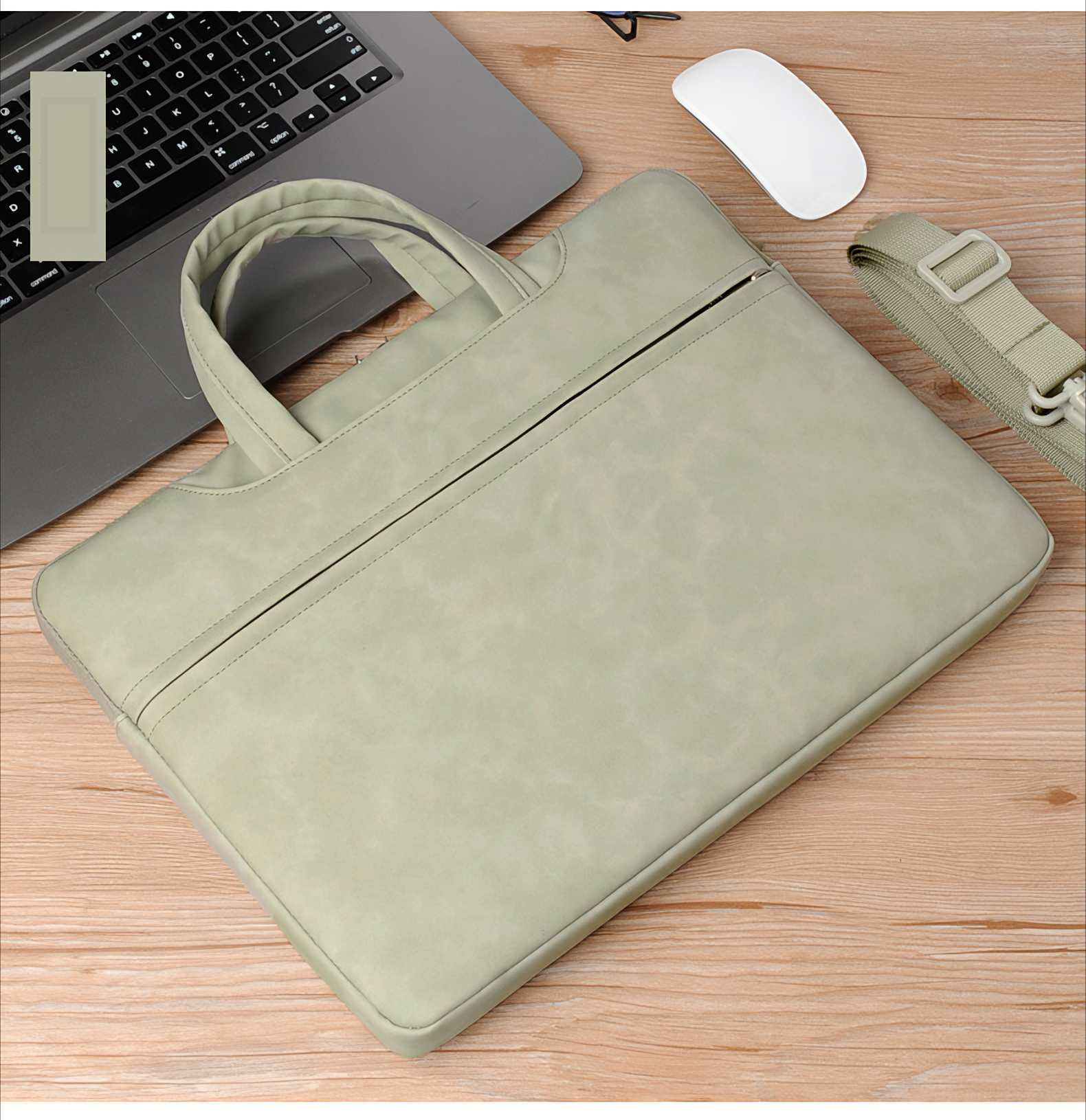 Eine Laptoptasche, ein Laptop und eine Maus liegen auf einem Holztisch. Die Tasche ist hellgrün, mit Griff und Schultergurt.