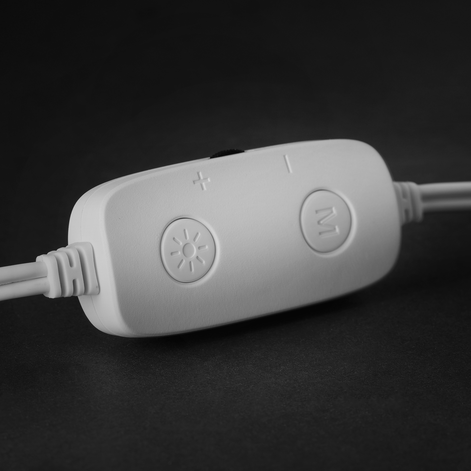 Un pannello di controllo bianco con pulsanti per luminosità, modalità e alimentazione. Sfondo nero. Due fili bianchi collegati.