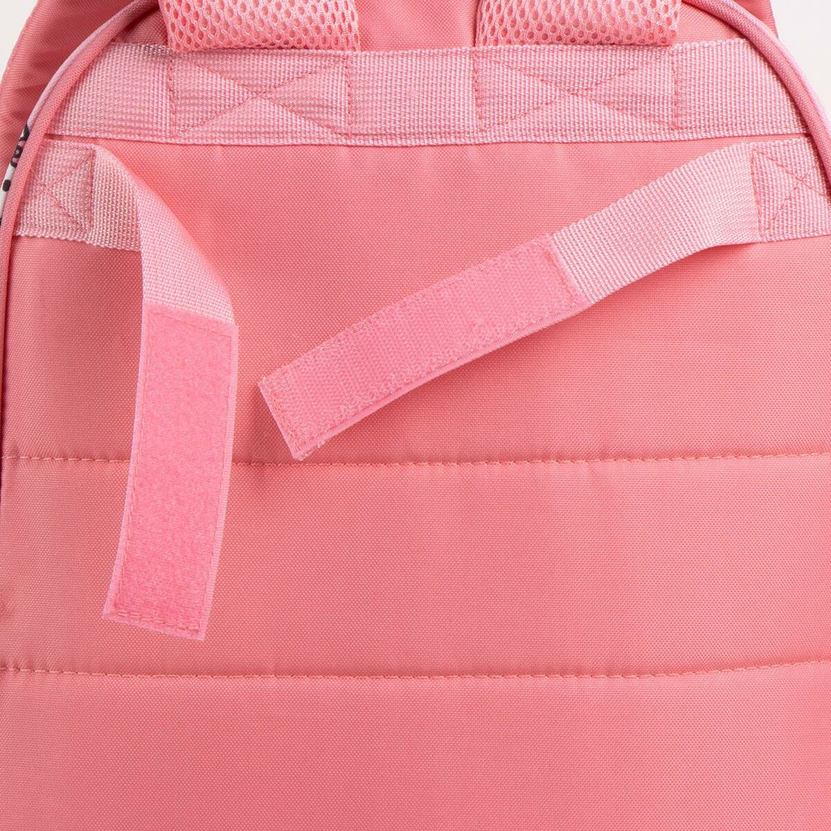 Nahaufnahme der Rückseite eines rosa Rucksacks. Sichtbare Gurte, Klettverschlüsse und gesteppter Stoff. Der Hintergrund ist einfarbig rosa.