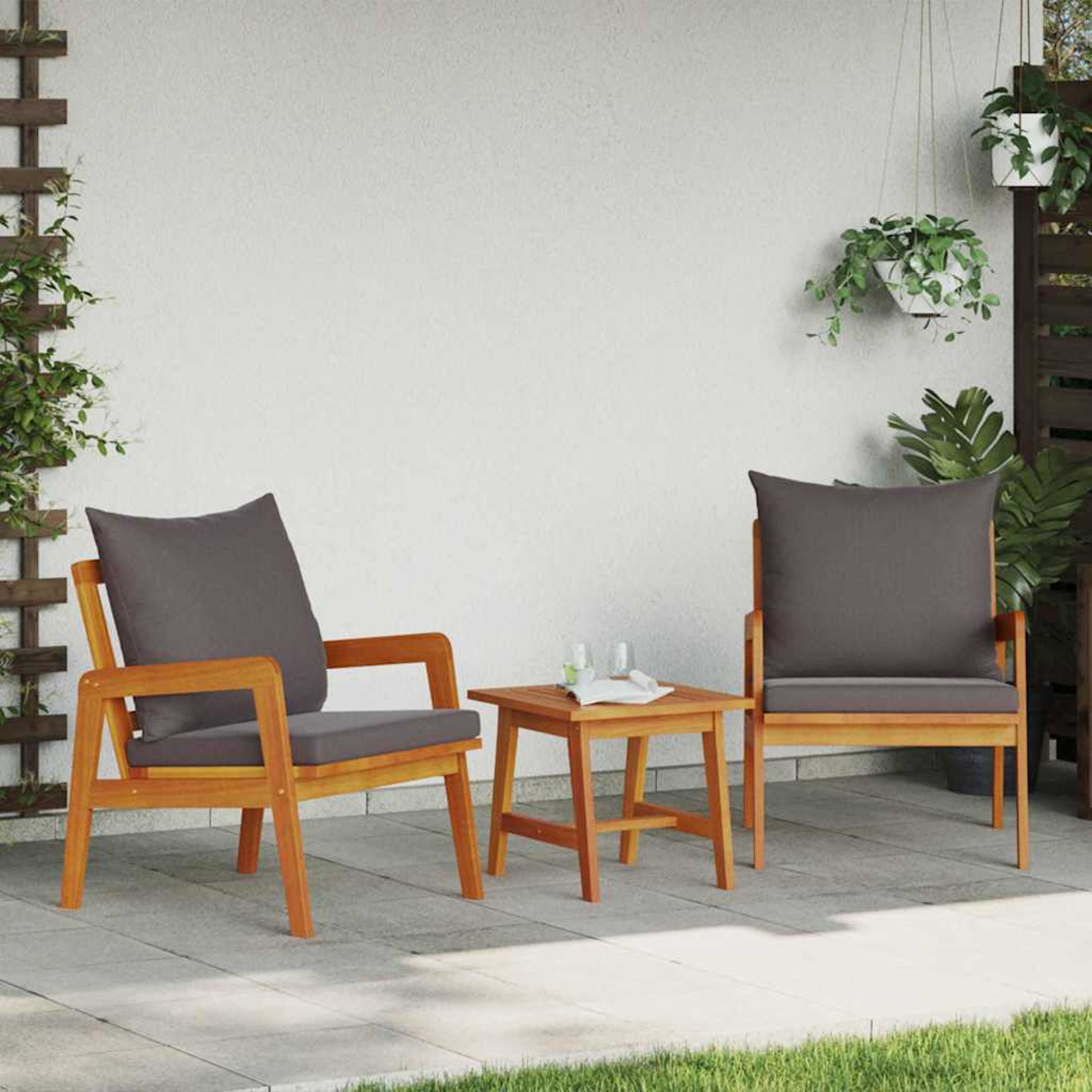 Zwei Holzstühle mit grauen Kissen und ein kleiner Tisch auf einer Terrasse, mit hängenden Pflanzen und einer weißen Wand im Hintergrund.