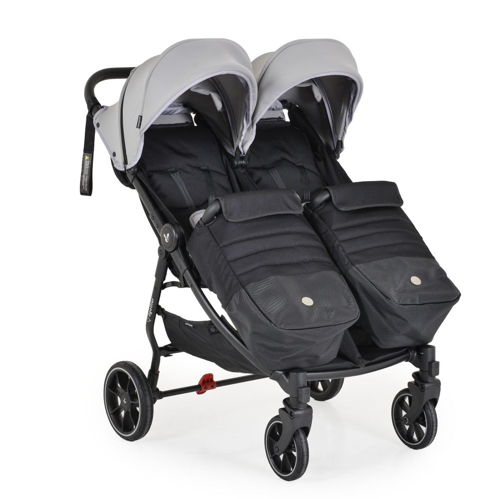 Ein Doppelkinderwagen mit schwarzen Sitzen, grauen Verdecken und schwarzem Gestell. Die Räder sind schwarz mit weißen Felgen. Der Hintergrund ist weiß.