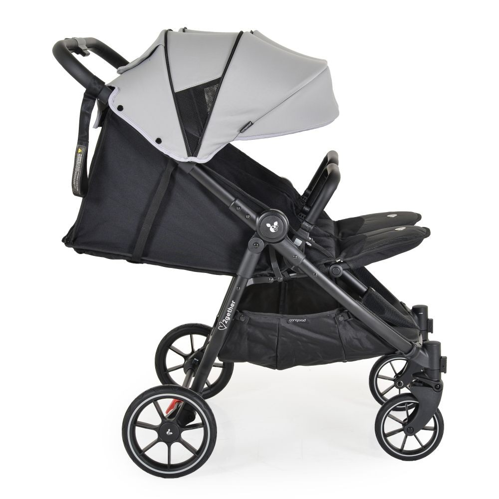 Ein schwarzer und grauer Zwillingskinderwagen. Er hat ein graues Verdeck, einen schwarzen Rahmen und Räder. Der Kinderwagen steht auf weißem Hintergrund.