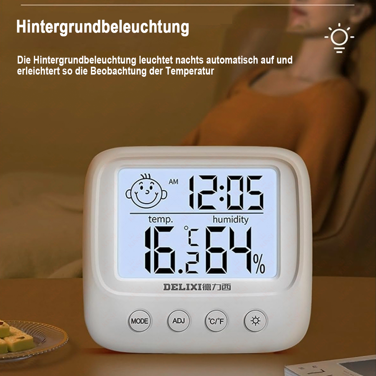 Eine weiße Digitaluhr zeigt Zeit, Temperatur und Luftfeuchtigkeit an. Im unscharfen Hintergrund sitzt eine Person. Die Uhr hat Knöpfe.