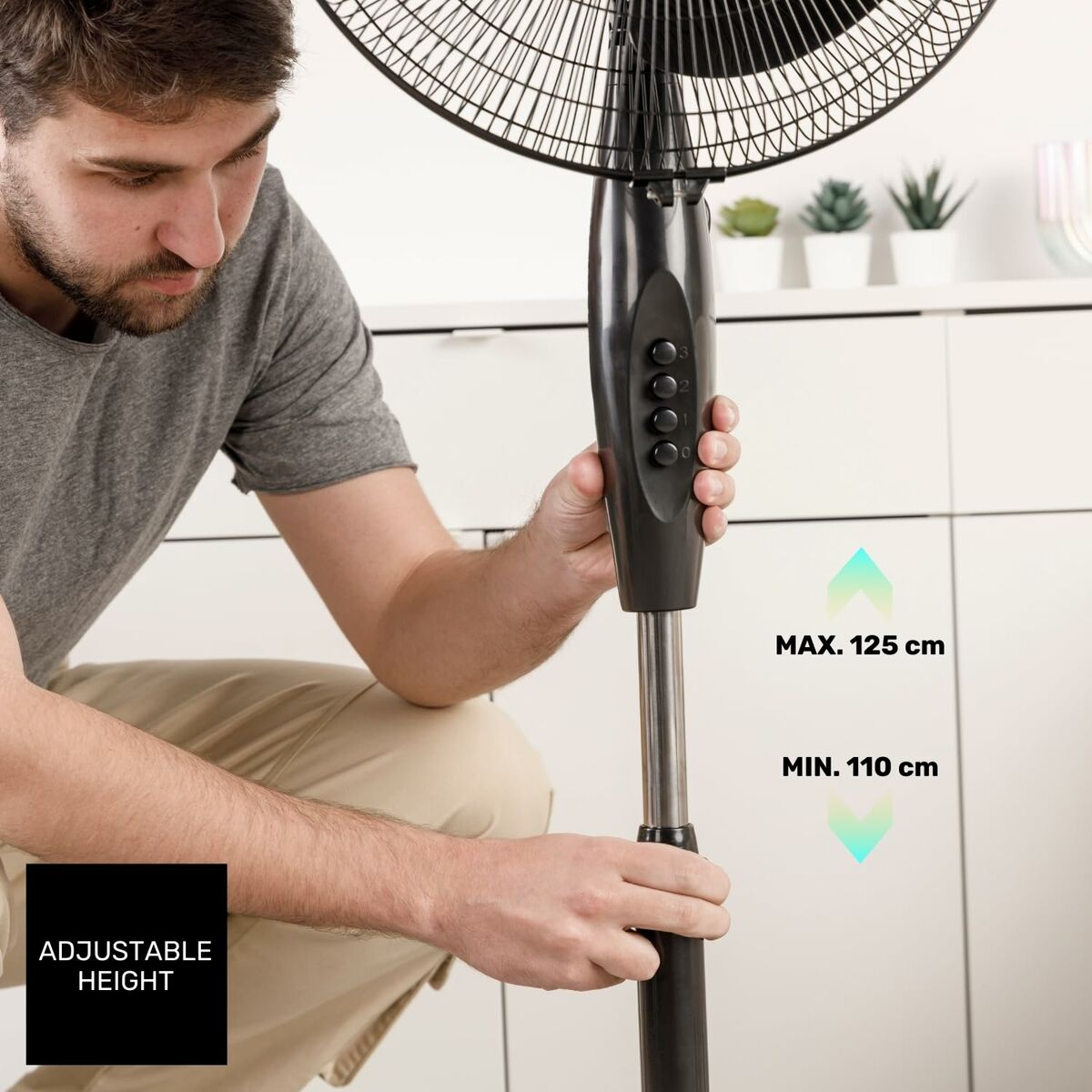 Mężczyzna reguluje wysokość czarnego wentylatora. Wentylator ma czarną kratkę i stojak. Wysokość jest regulowana w zakresie od 110 do 125 cm.